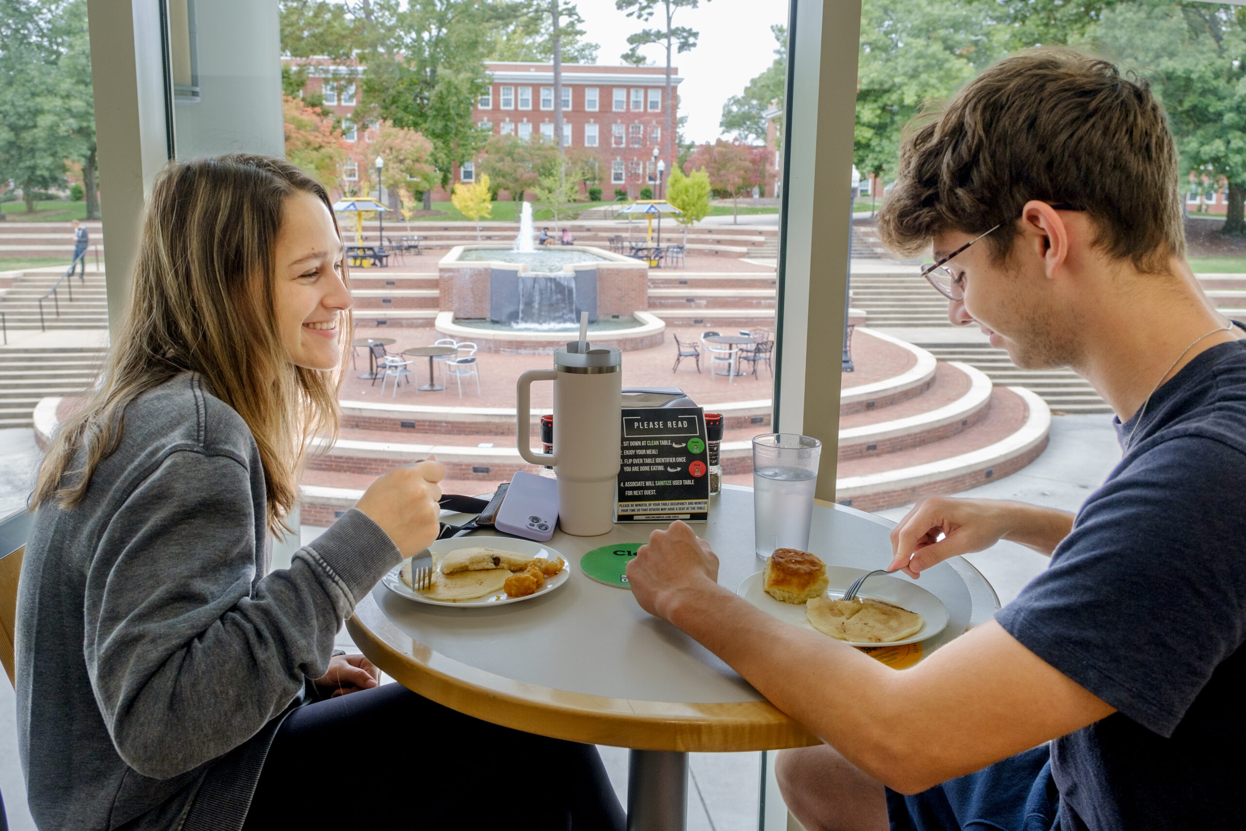 First year students Dianna Liana and Austin eat at a table in the UNCG dining hall.
