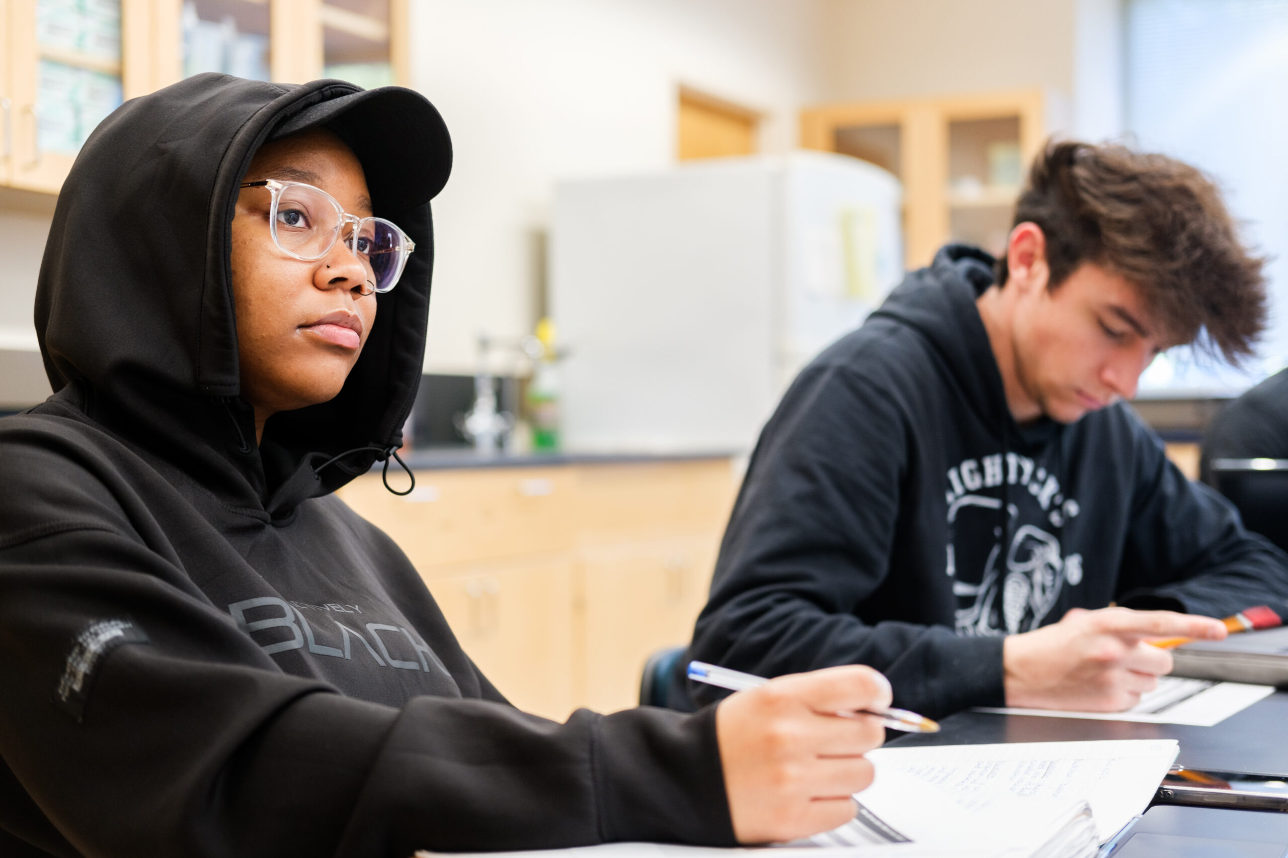 Two students in a science lab room take notes.