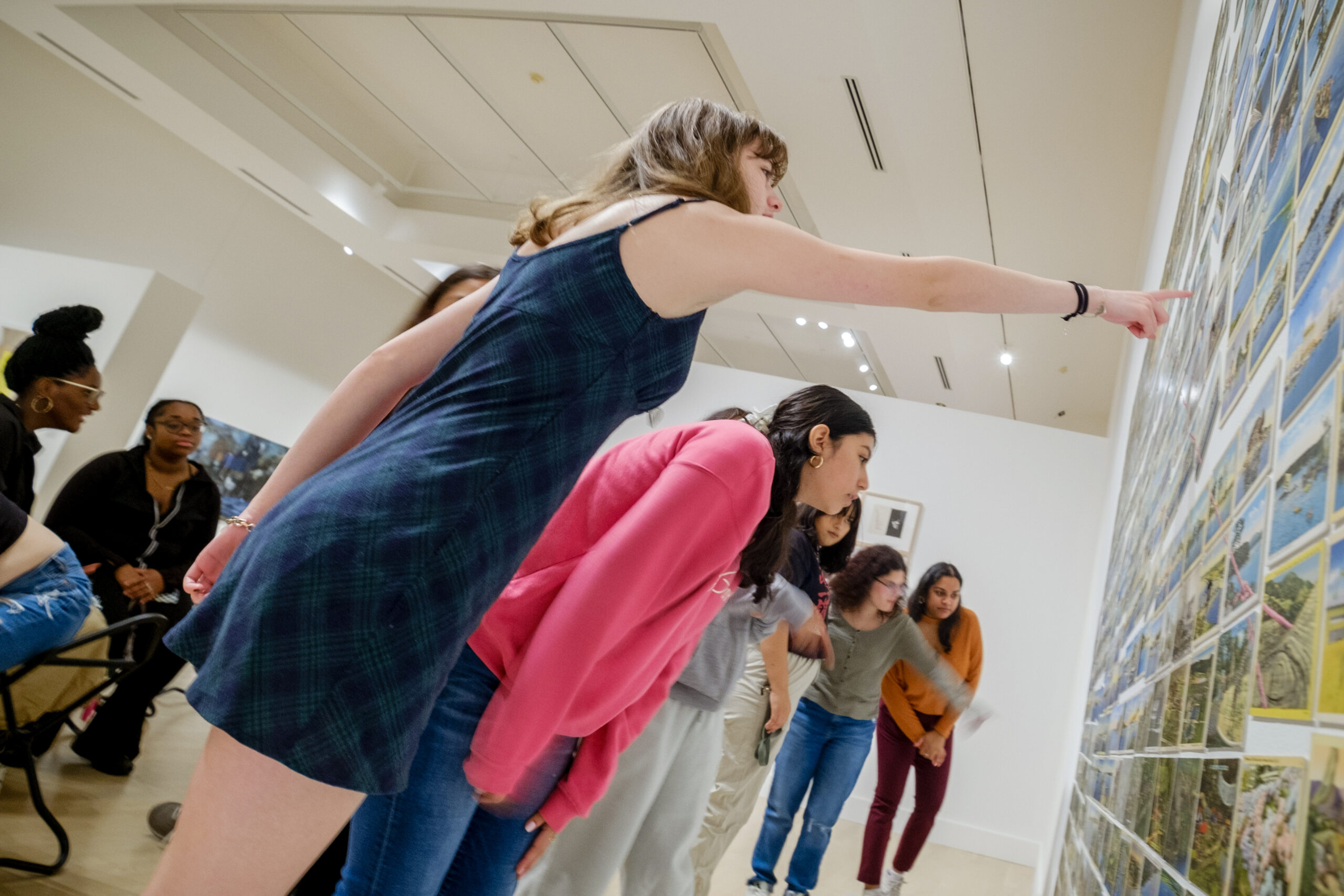 Student points at a piece of artwork on the wall of a gallery. The artwork is not visible.