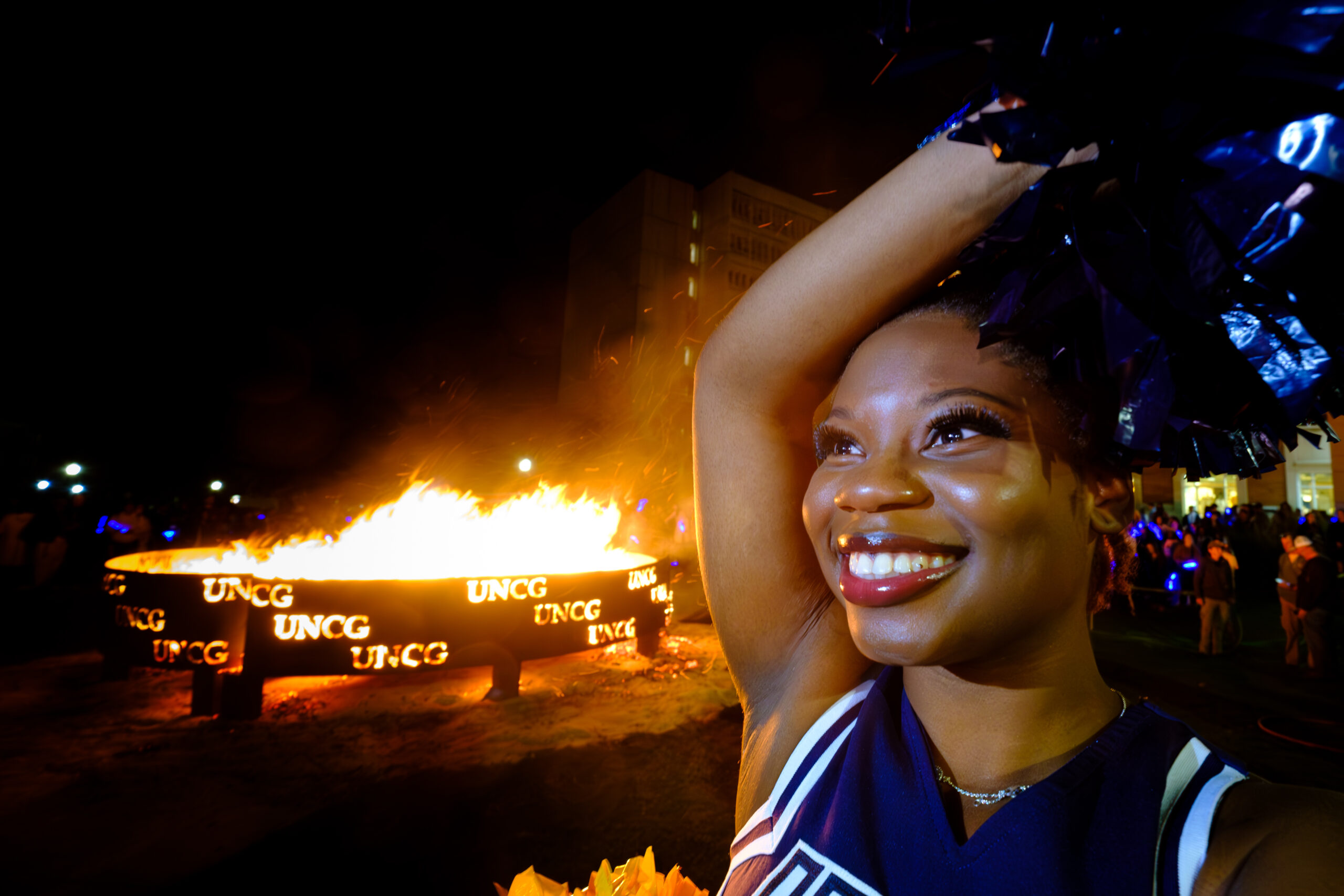 A UNCG has her arm up in front of the 2023 Homecoming bonfire