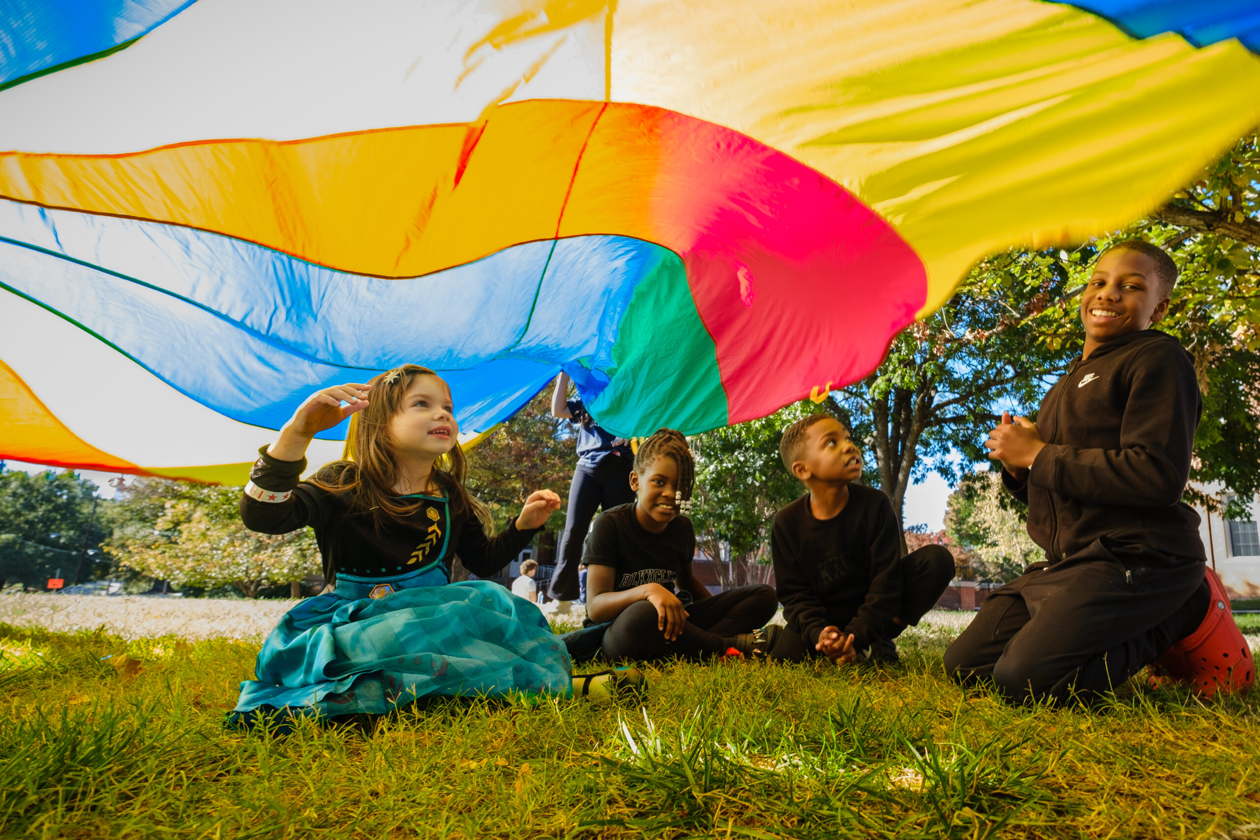 Four children gather under a colorful parachute at the Children's Festival.
