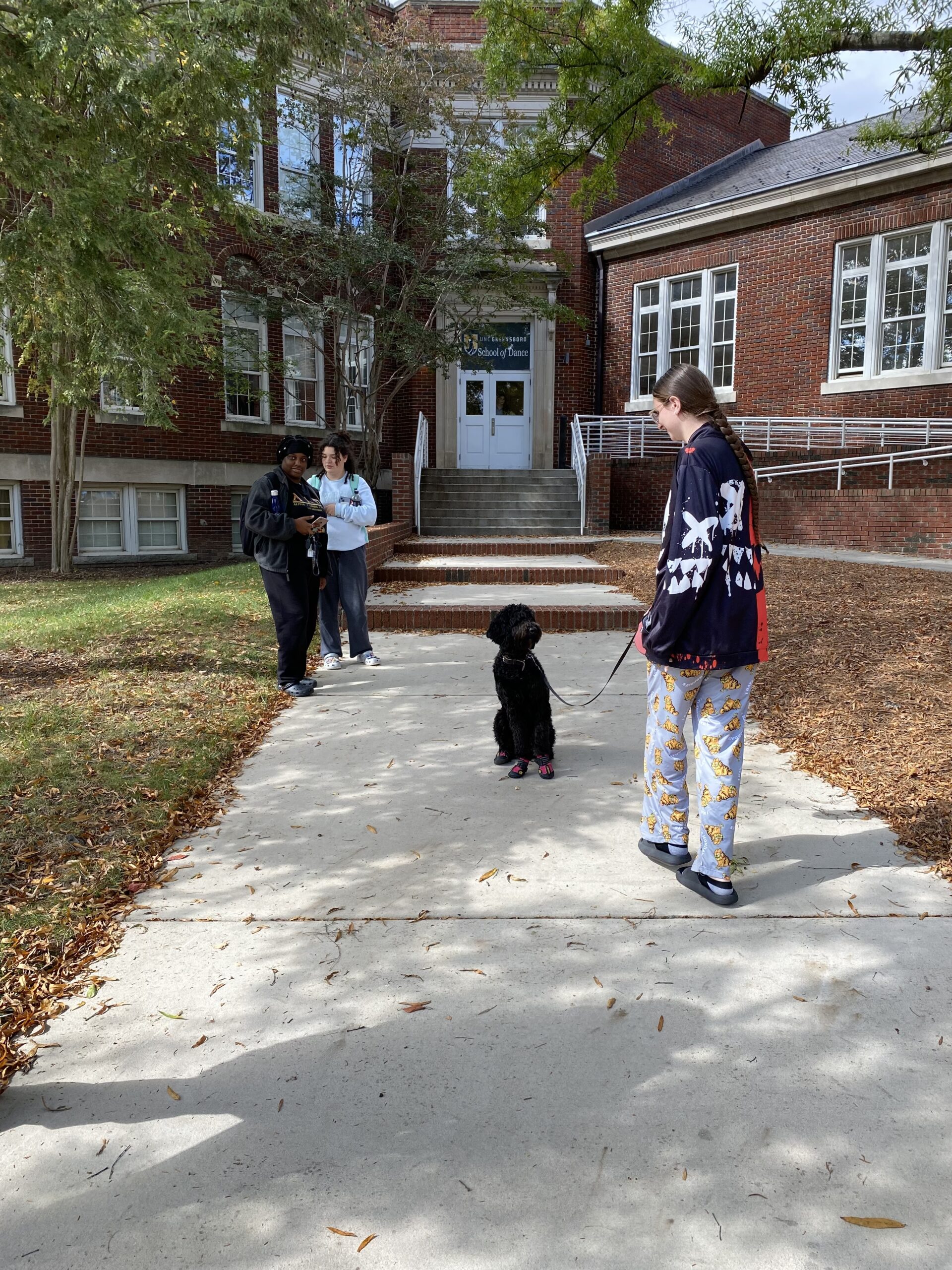 Student walks large black dog in front of School of Dance building.