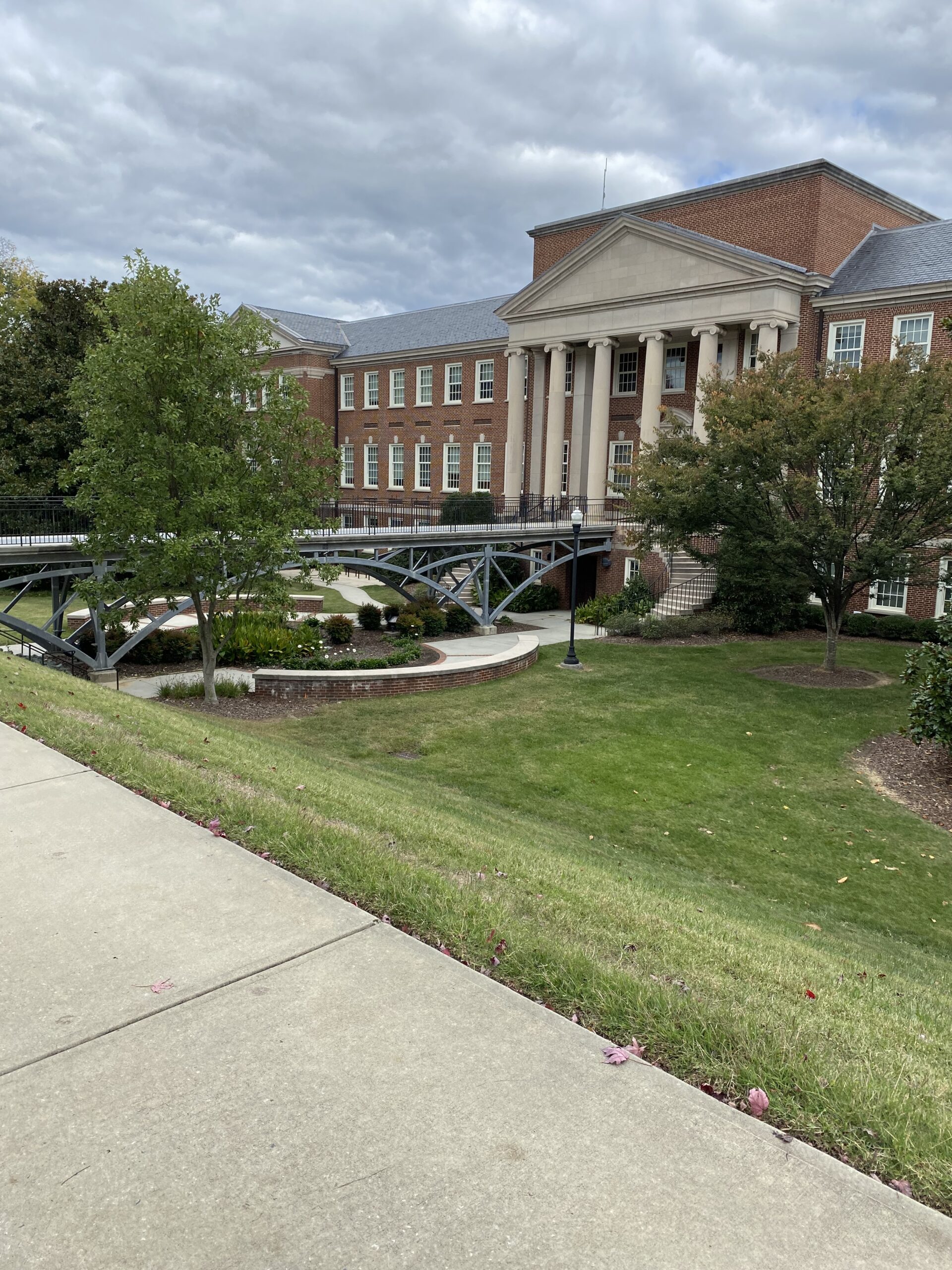 View of the UNCG Petty Building, a brick building with a bridge leading to it over a grassy area