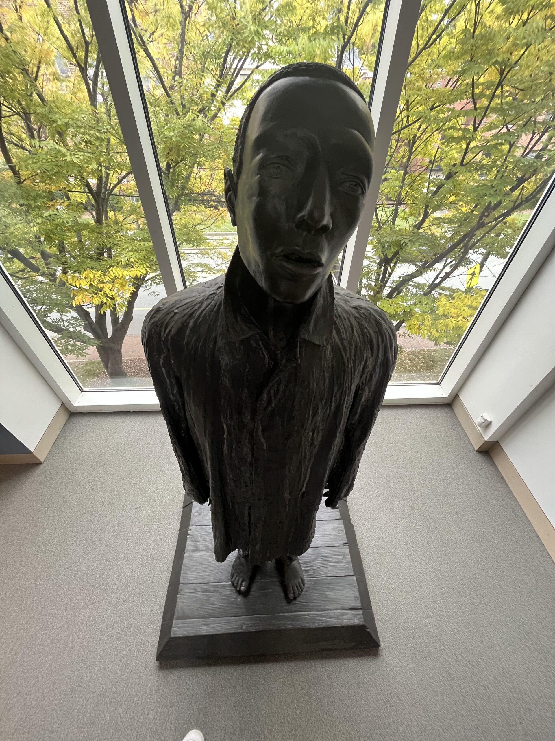 Top-down view of a life-sized sculpture of a figure in a long coat.