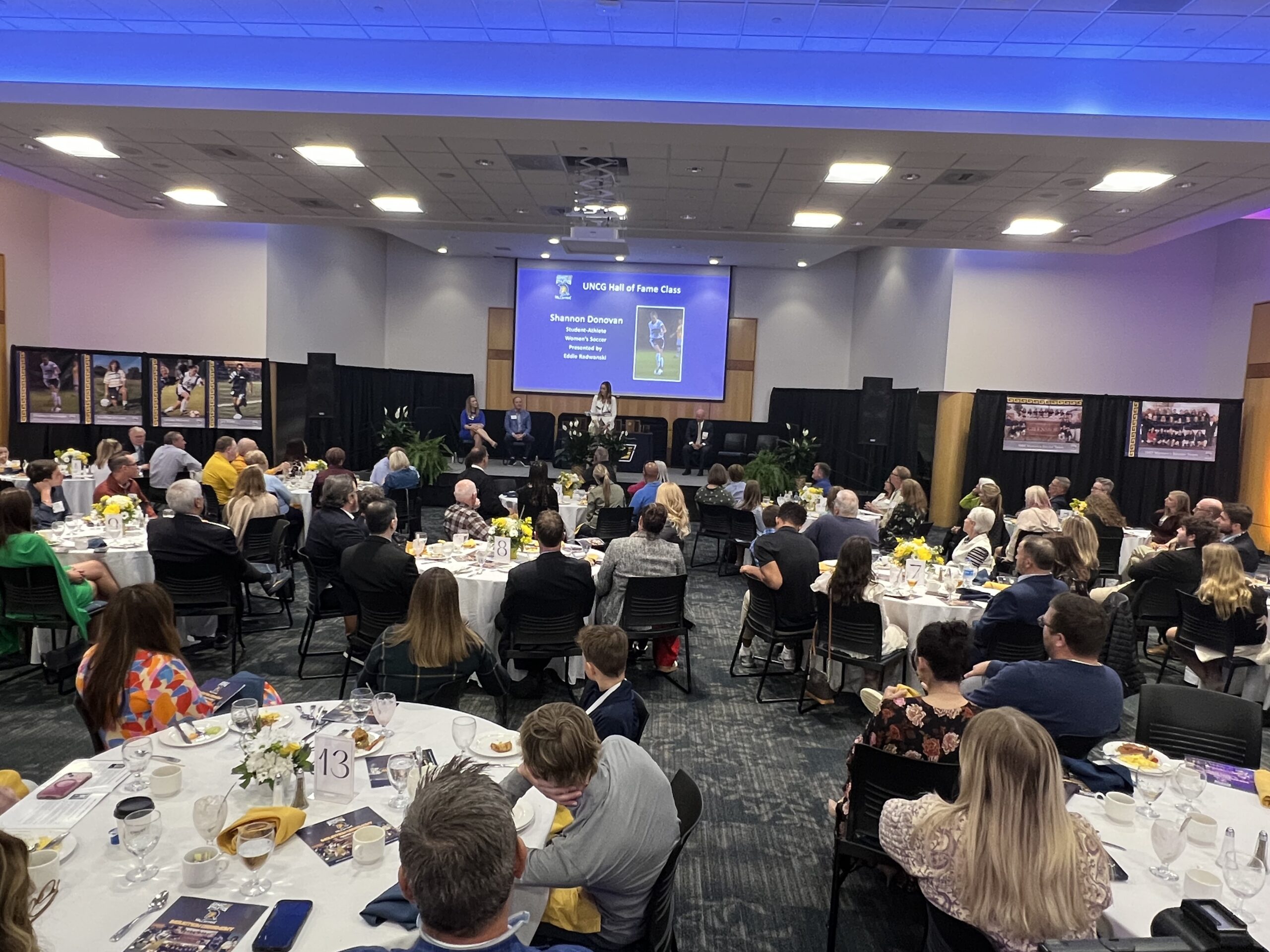 Athletics hall of fame event in Cone Ballroom, people seated during presentation.