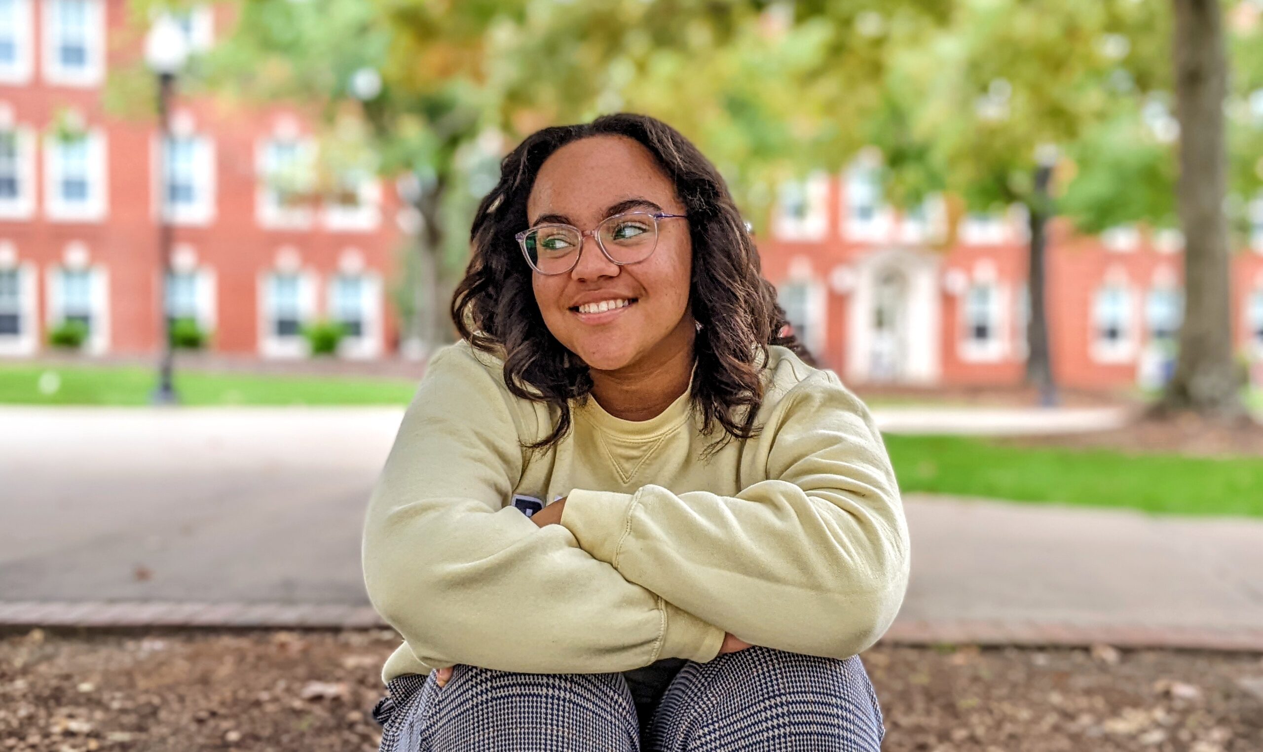 A UNCG student in a sweater sits outside enjoying the fall air.