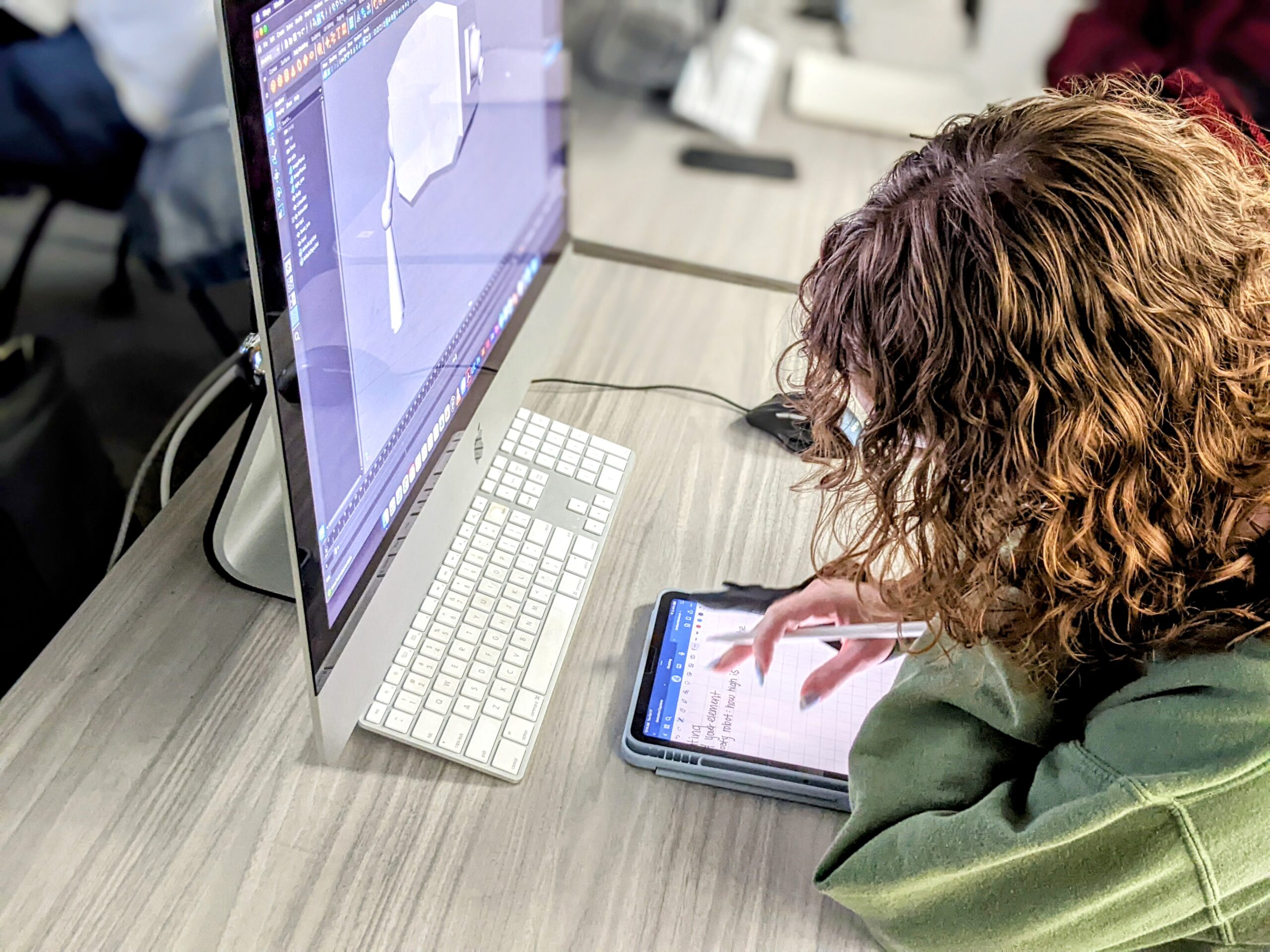 Student sits at a monitor hovered over a tablet taking notes.