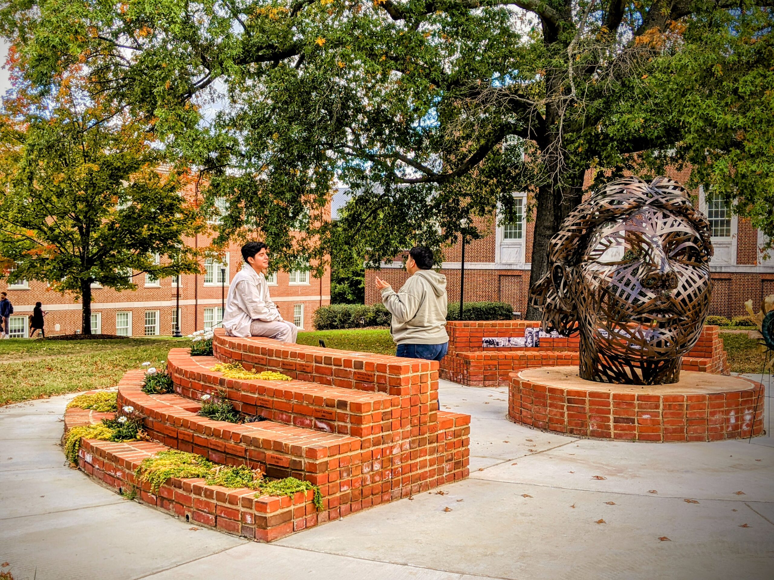 Two students having a conversation at the WC Tribute sculpture, Astera on College Avenue.