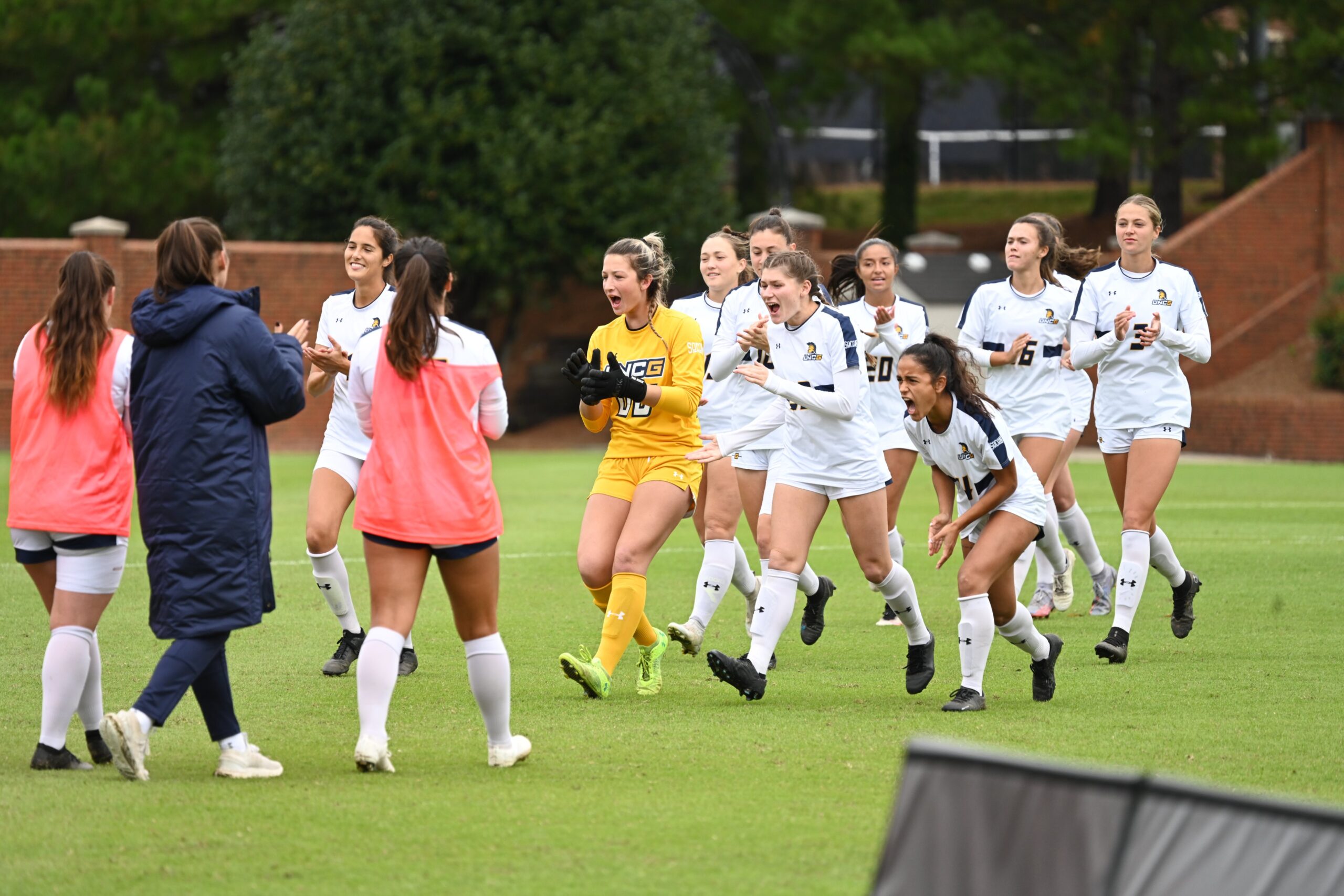 UNCG women's soccer players clap and smile as they run across the field.