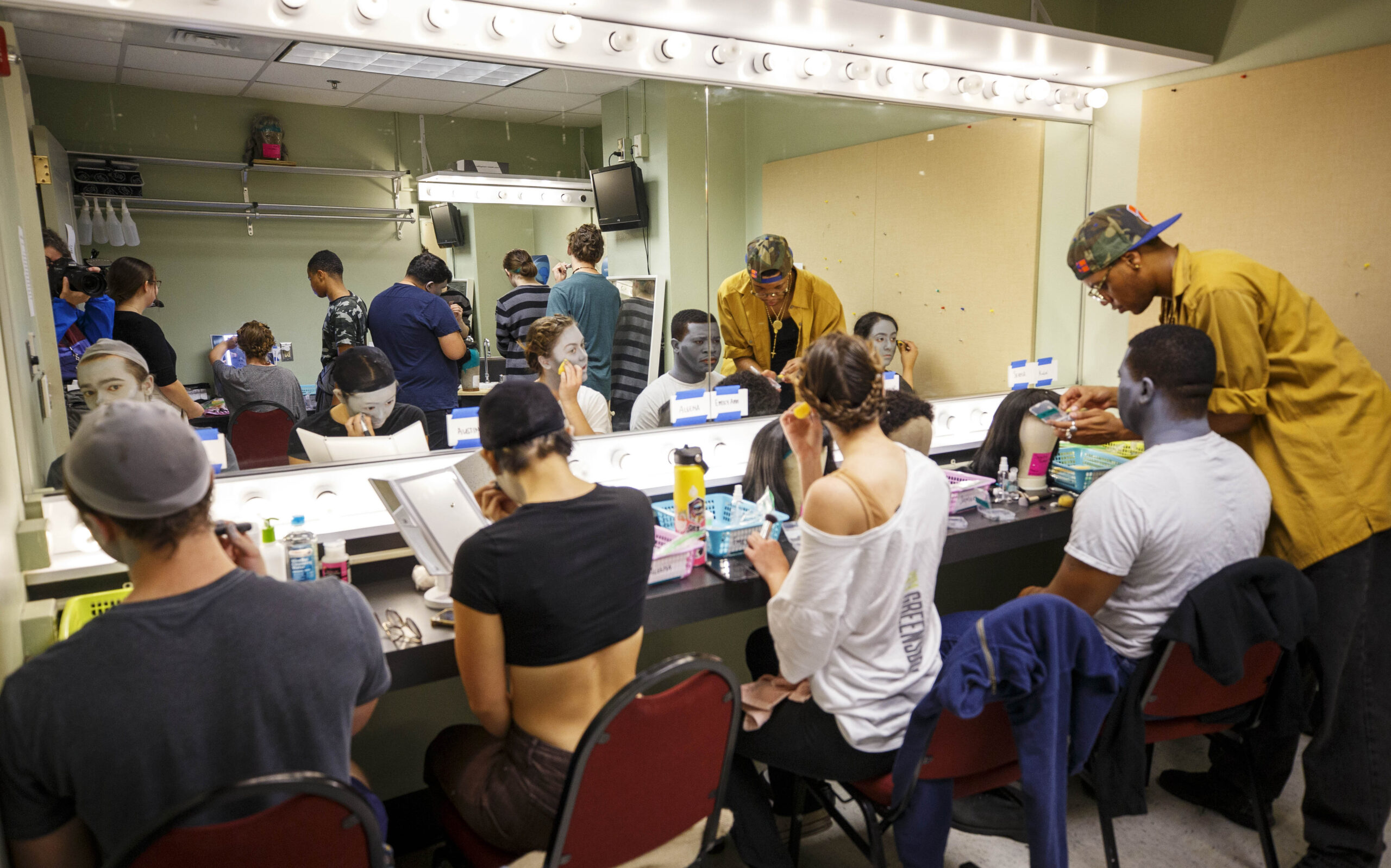 Actors work on hair and makeup in a dressing room.