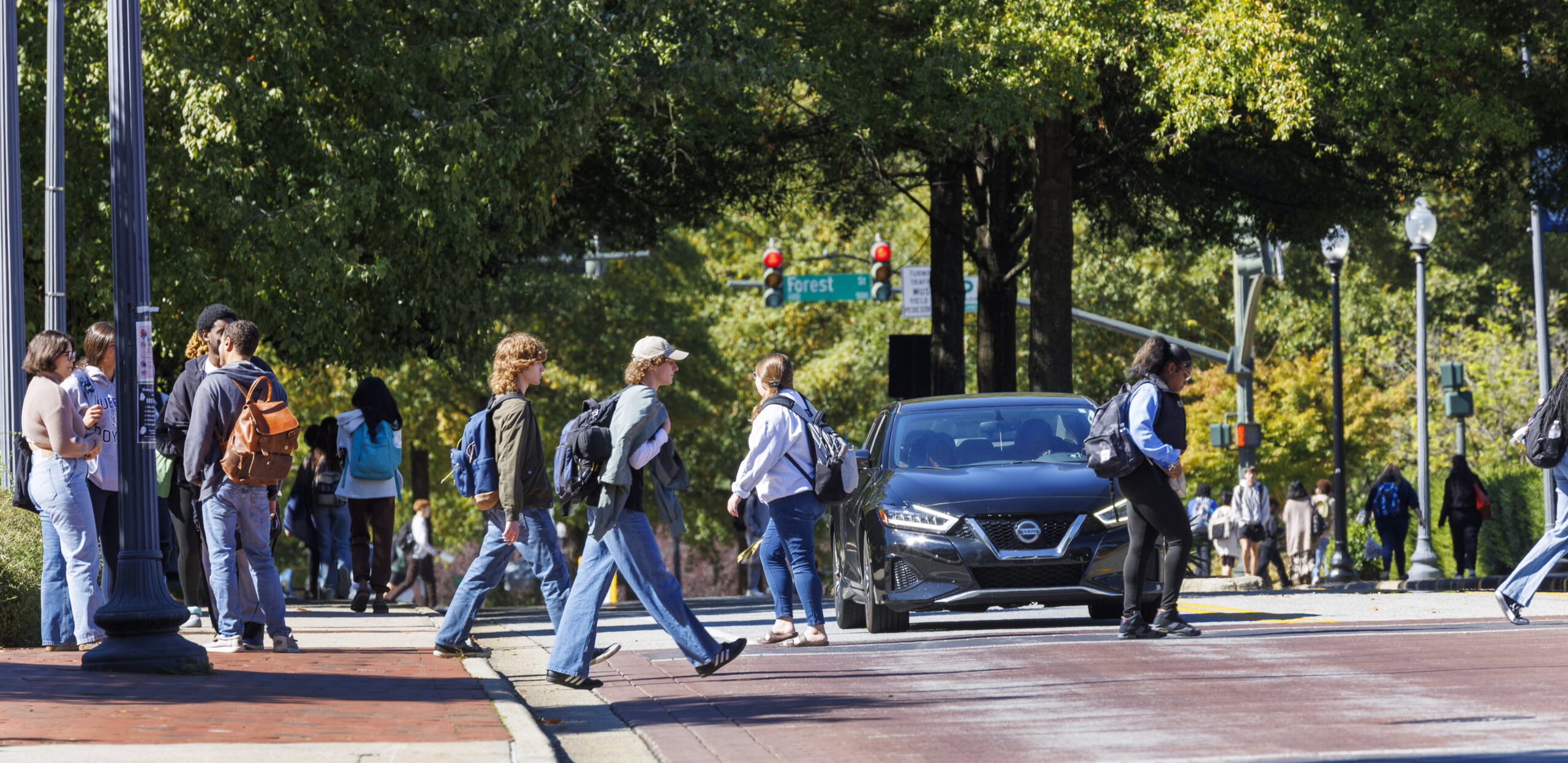 Students walk through a street crossing at UNCG while a car waits at a red light.