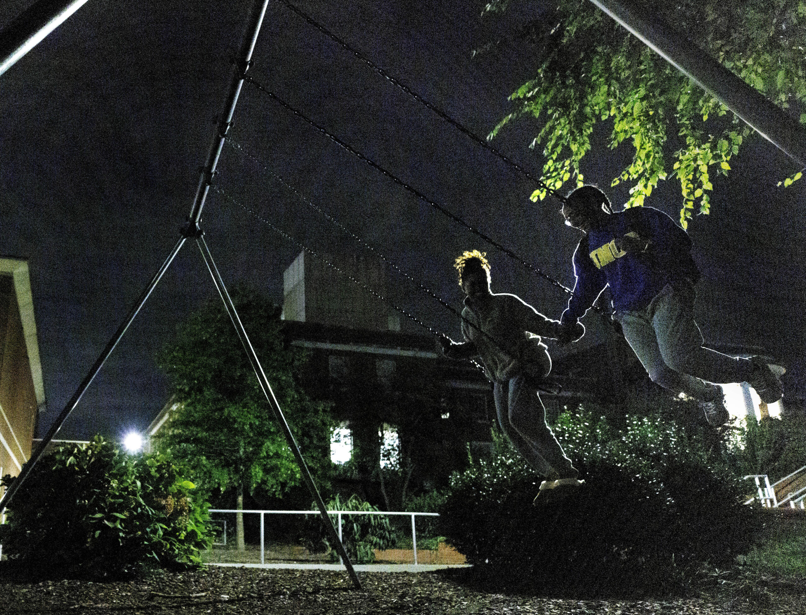 Two UNCG students, hold hands while swinging on a swing set at night.