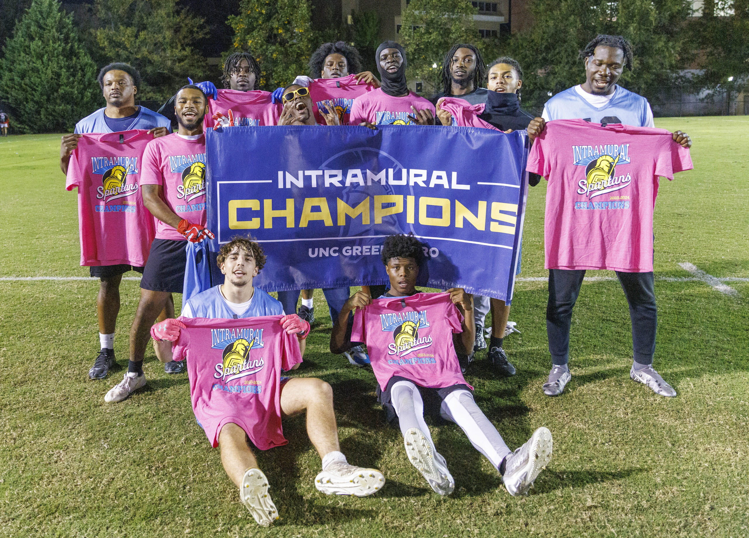 The championship flag football team poses holding pink tshirts and "intramural champions" flag.