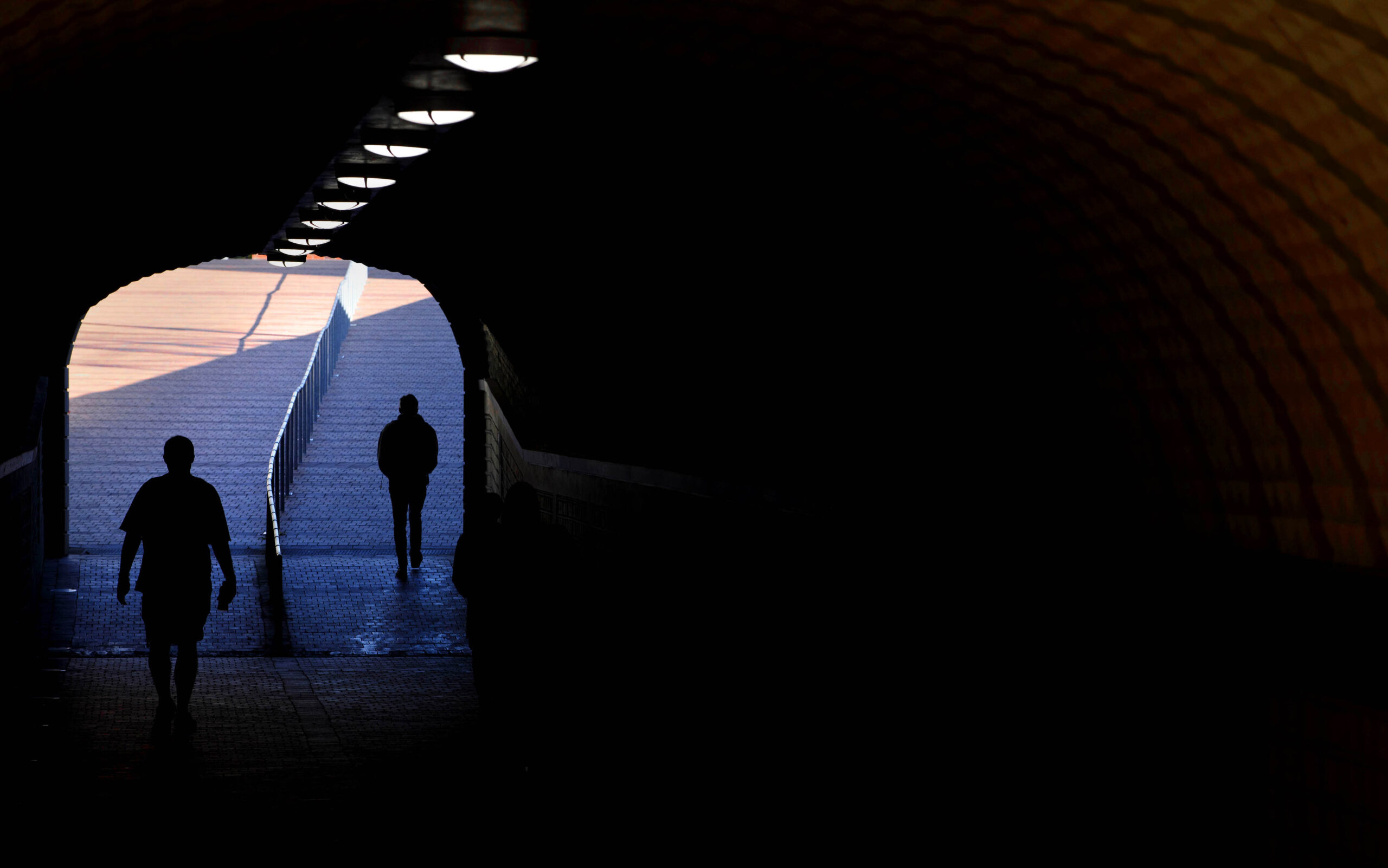 Silhouettes of students at the bright end of a dark underpass.