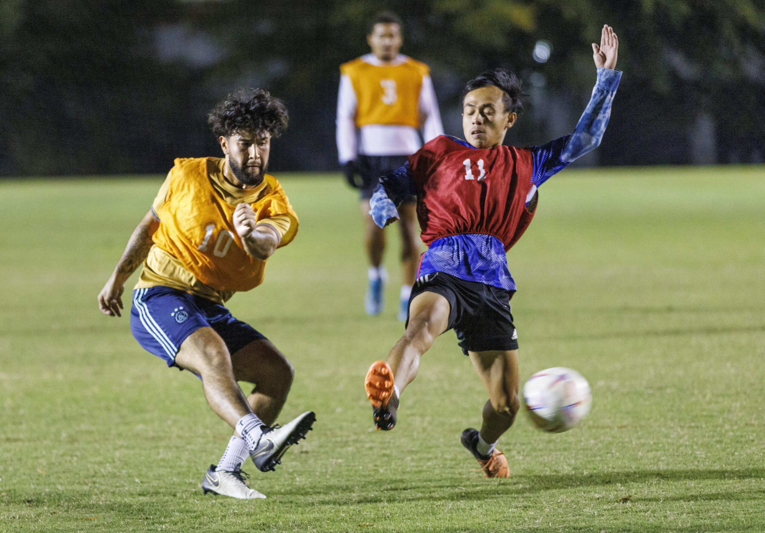 Intramural soccer players wearing red and yellow bibs fight for the ball