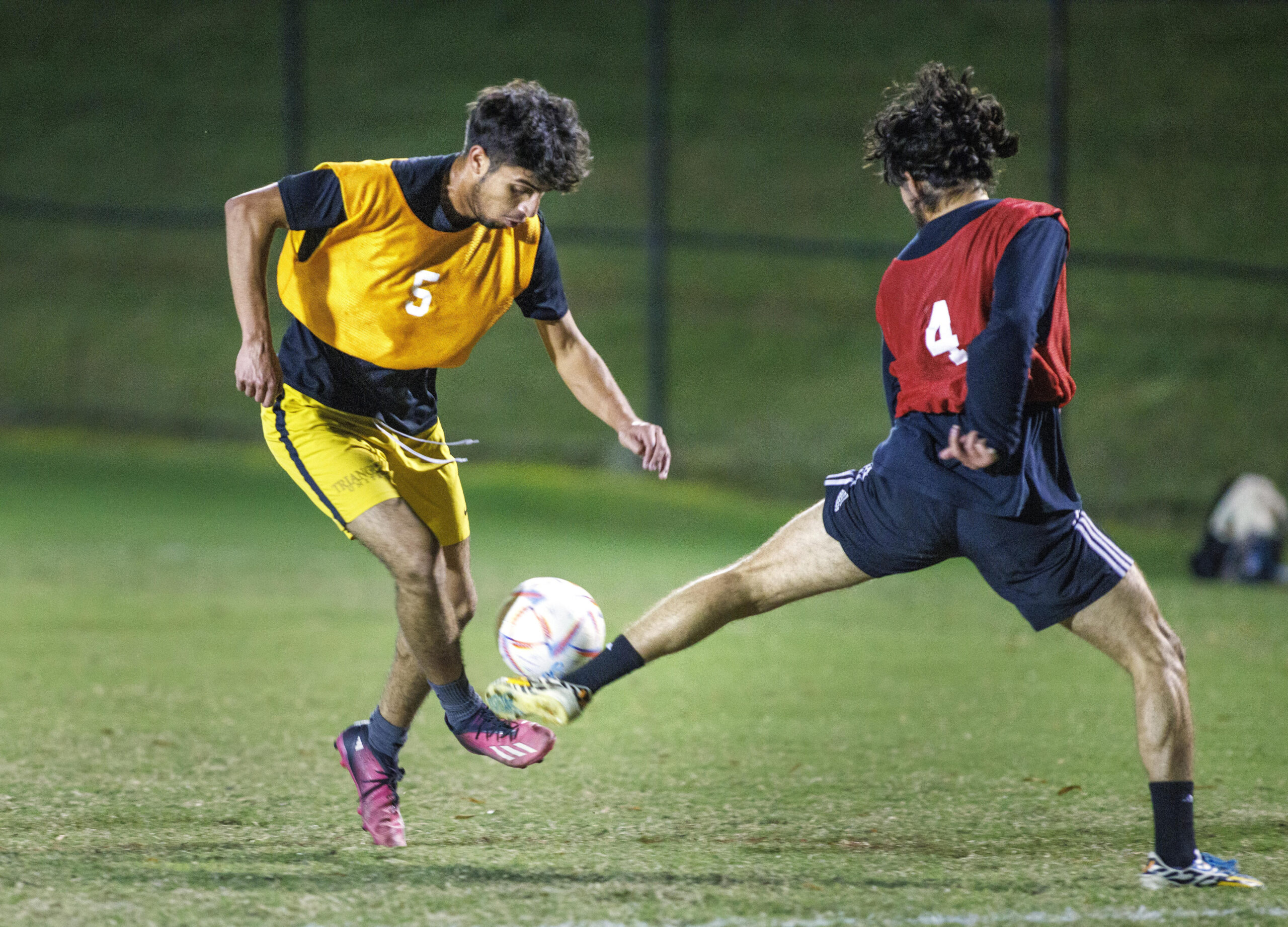 Intramural soccer players wearing red and yellow bibs fight for the ball