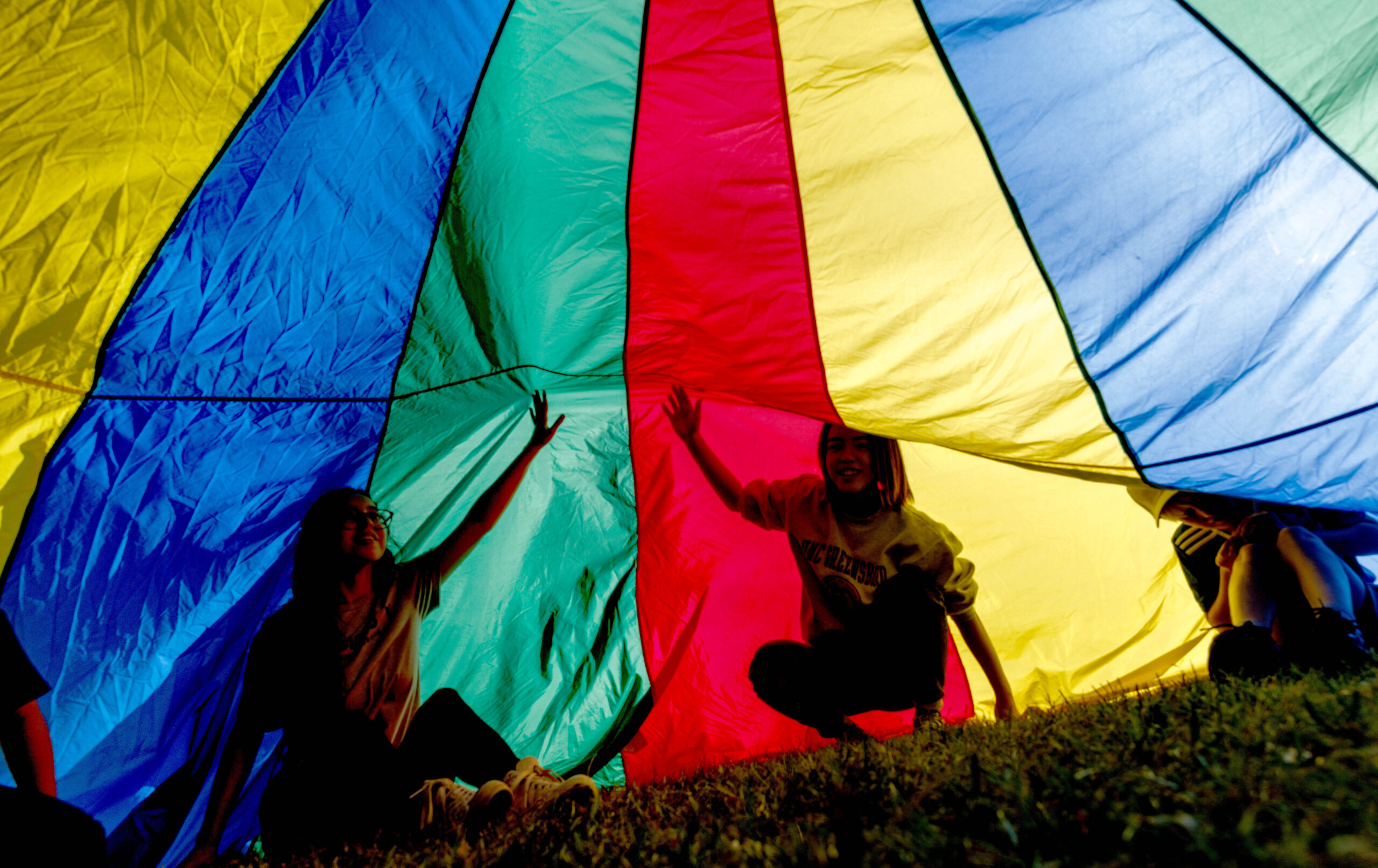 Children play under a colorful parachute.