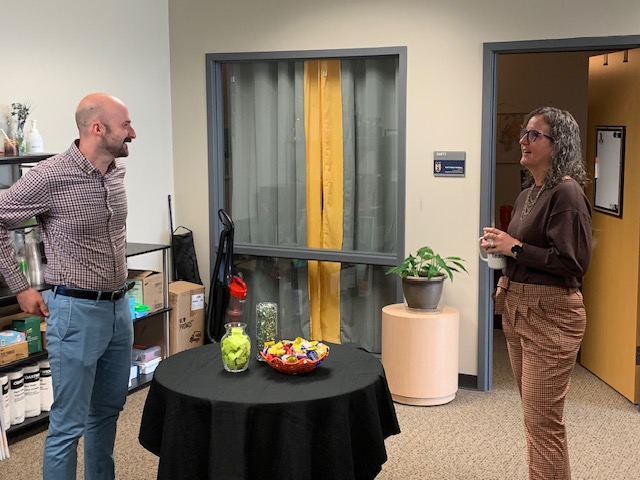 Two people stand around a table and talk.