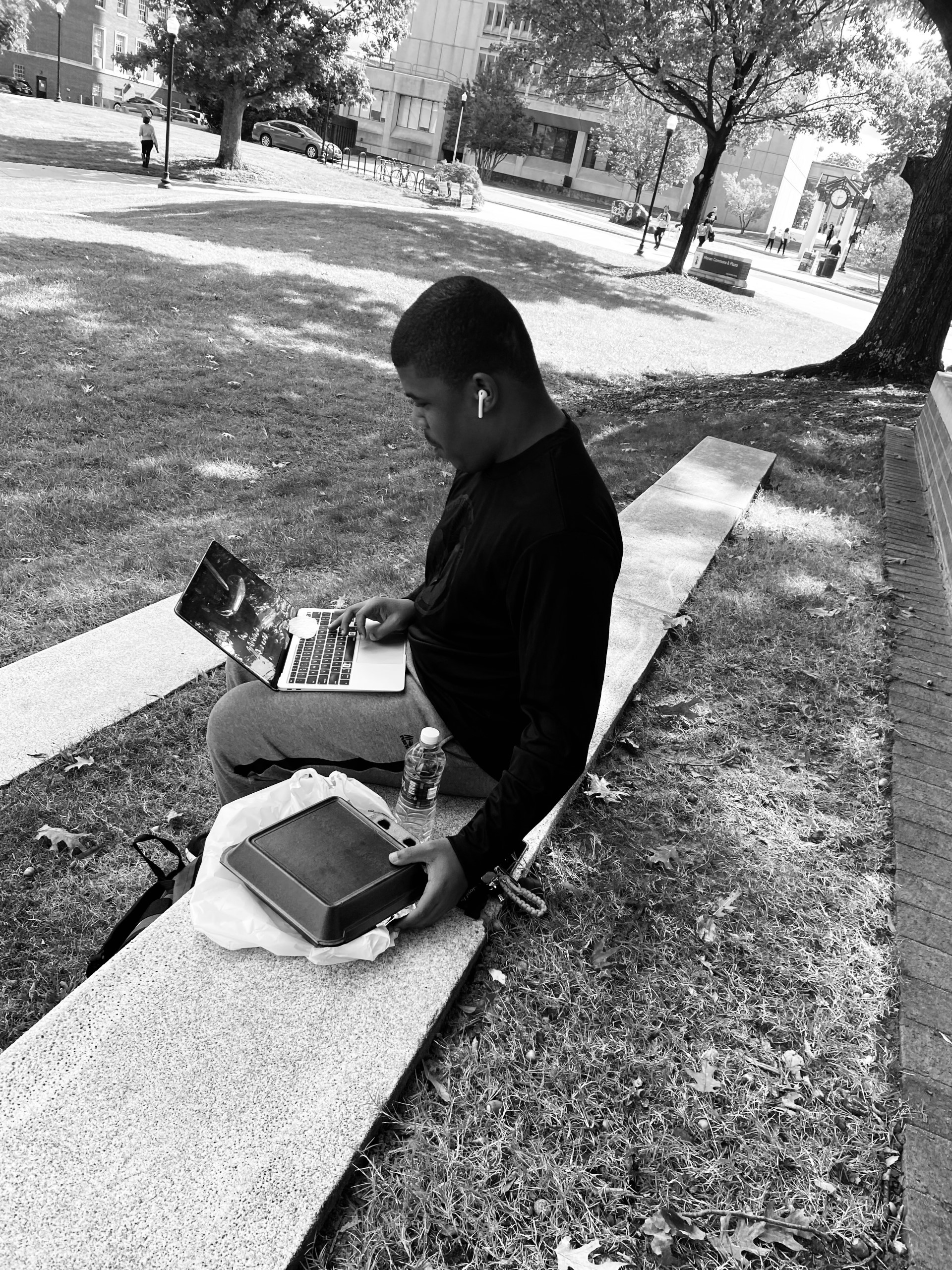 A UNCG student eats lunch outside and works on his laptop.