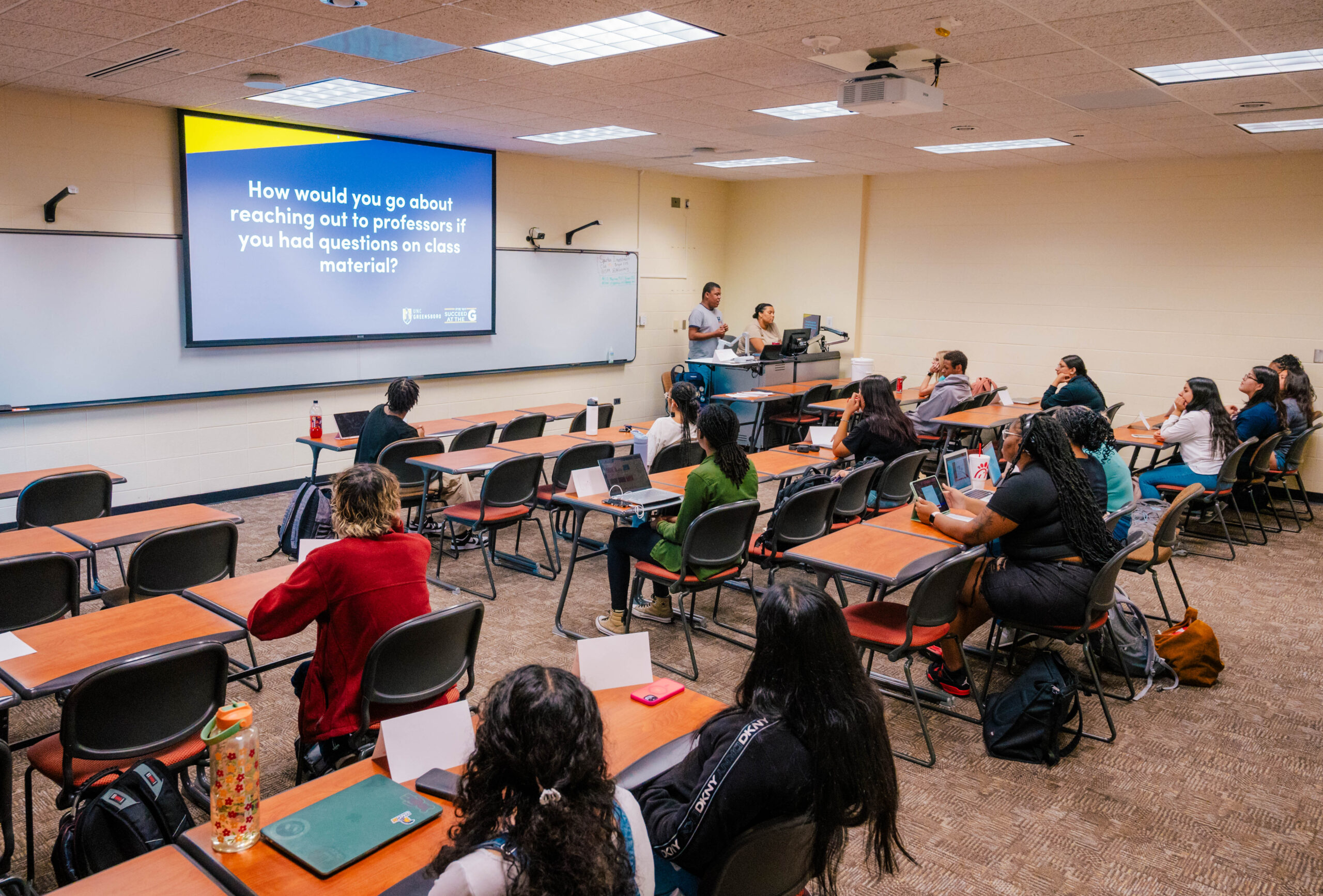 Students in classroom with presentation on screen in the background.