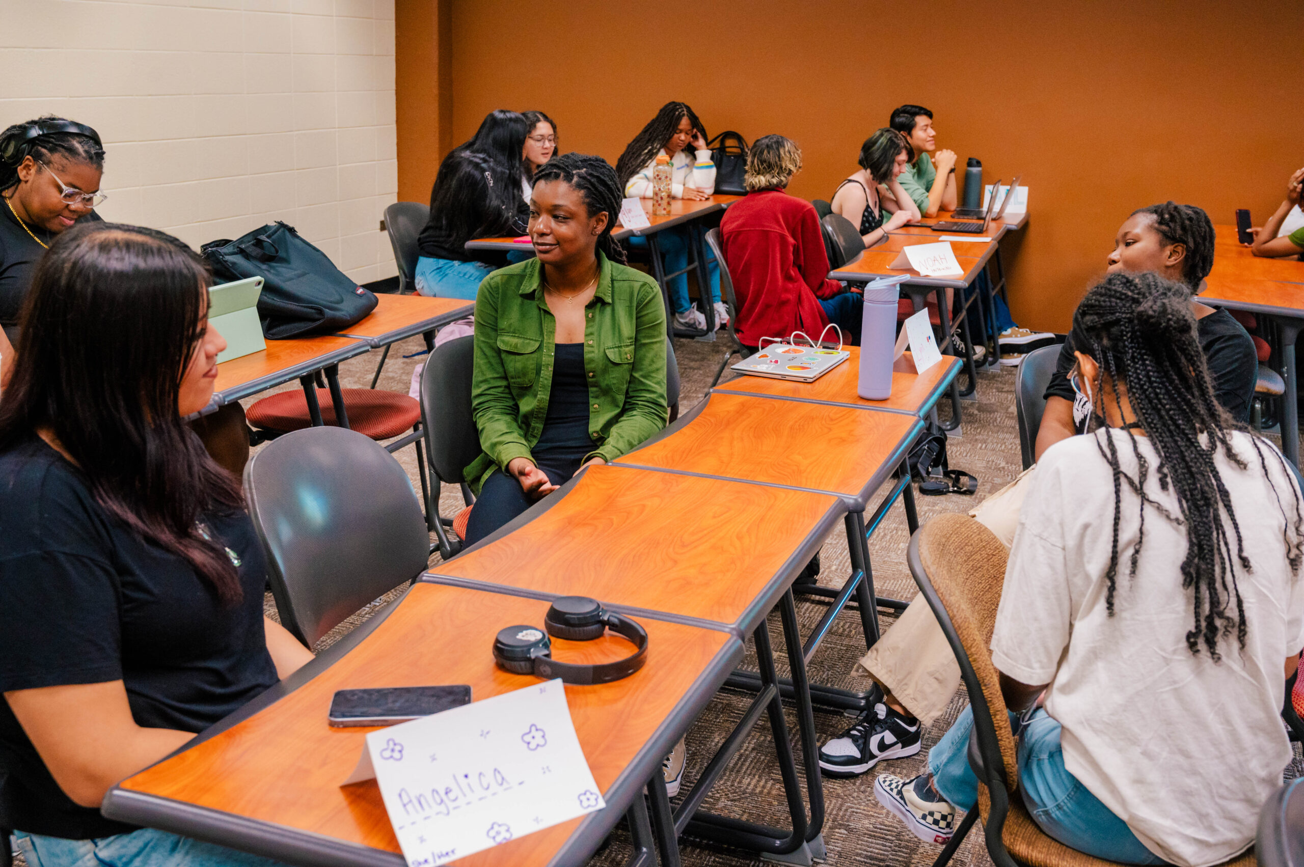 Students talk in groups at tables in a classroom.