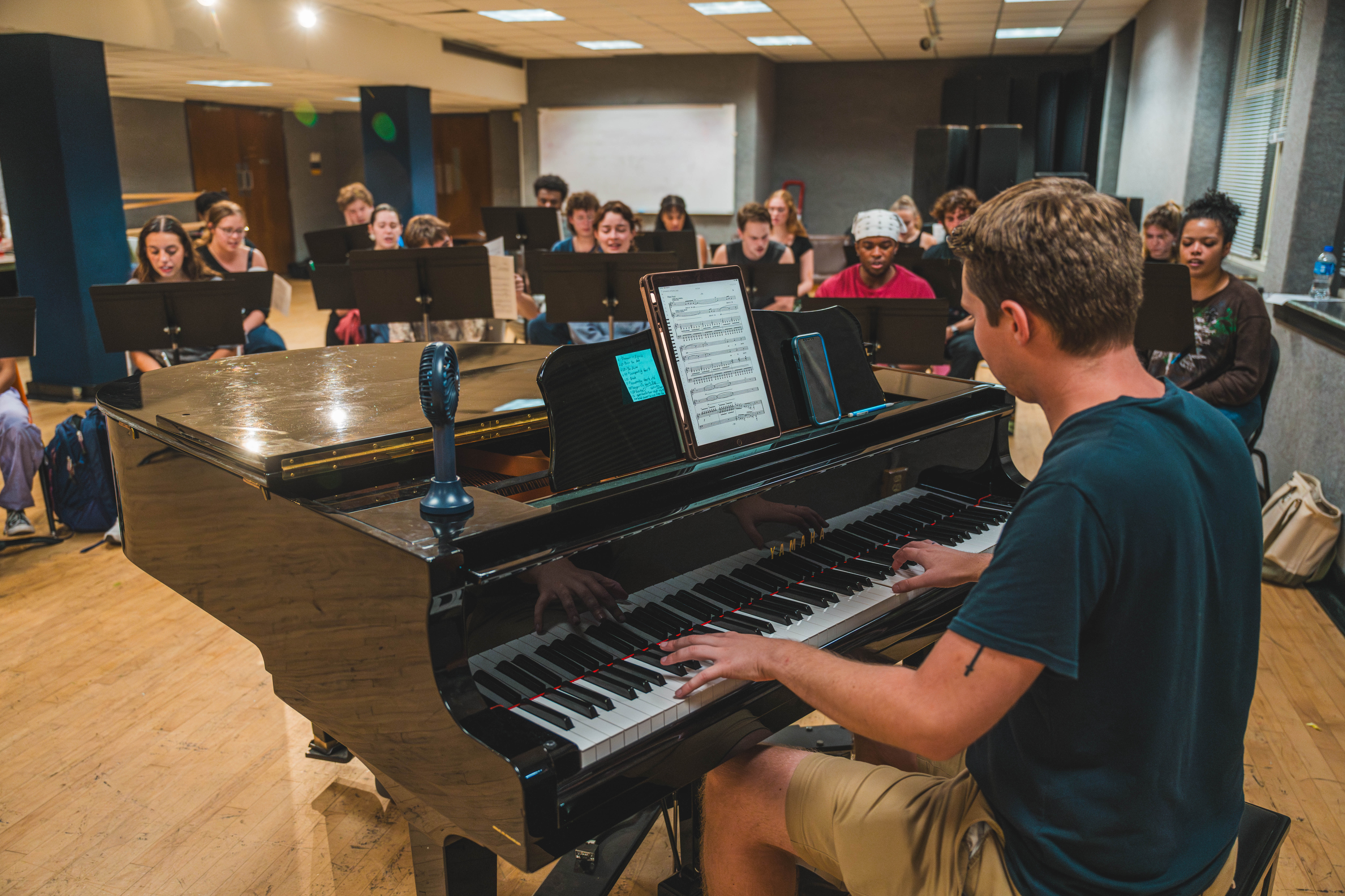 Student seated at a piano performs with other students.