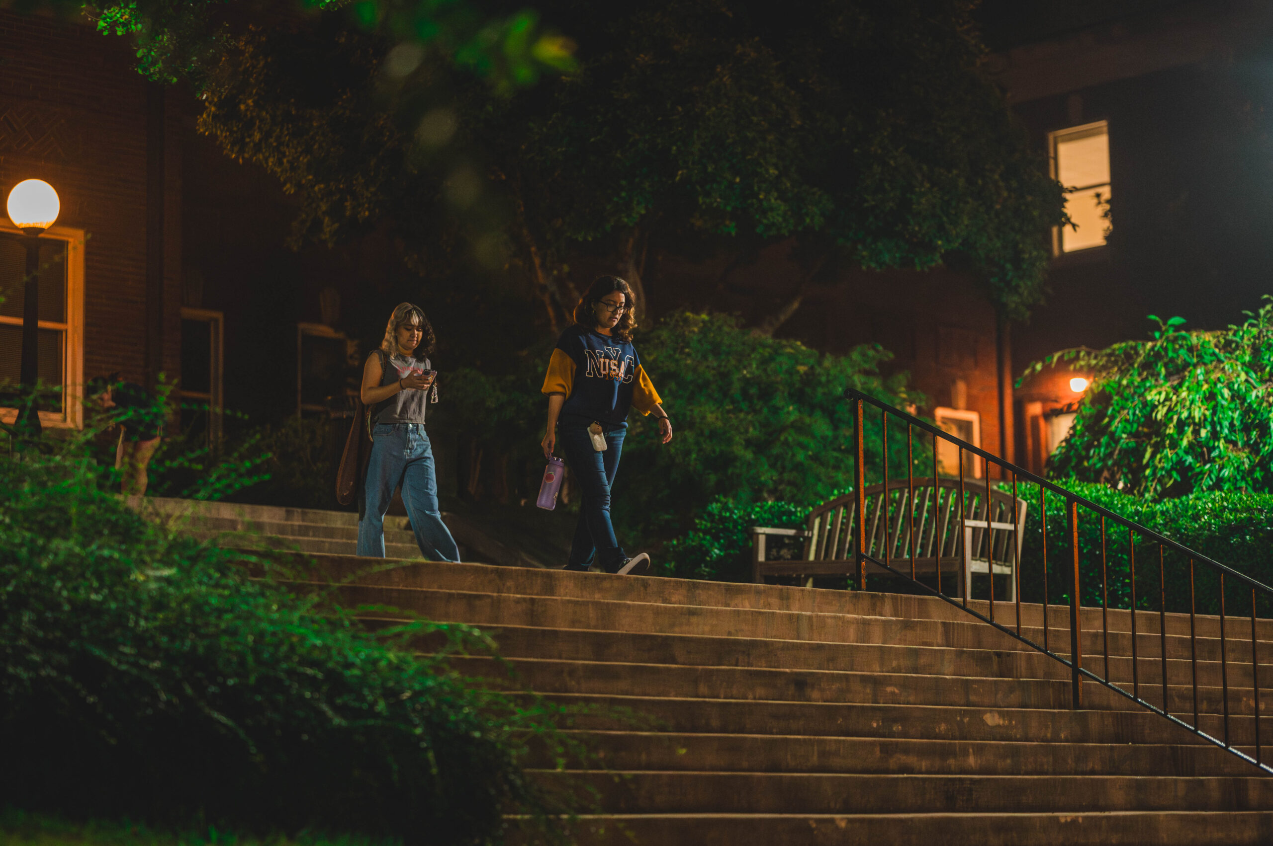 Two students walk down steps of the Curry building on UNCG's campus at night.