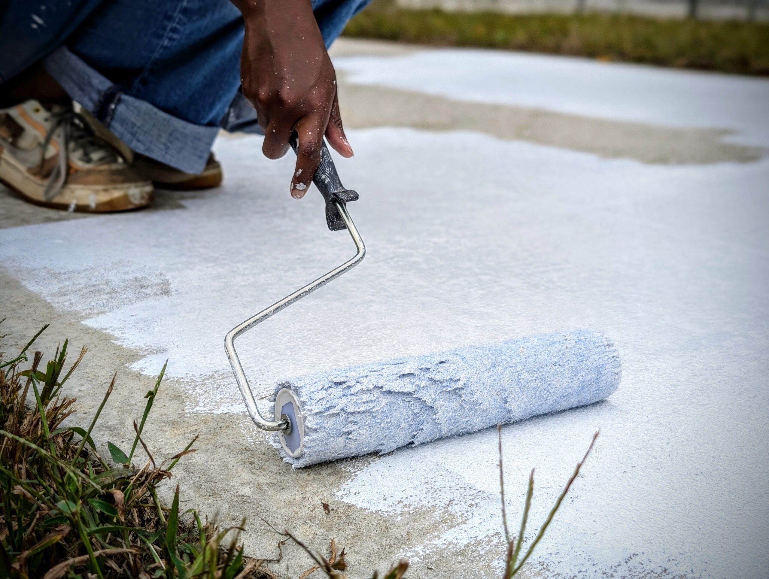 Close-up of a hand rolling white paint onto a sidewalk.