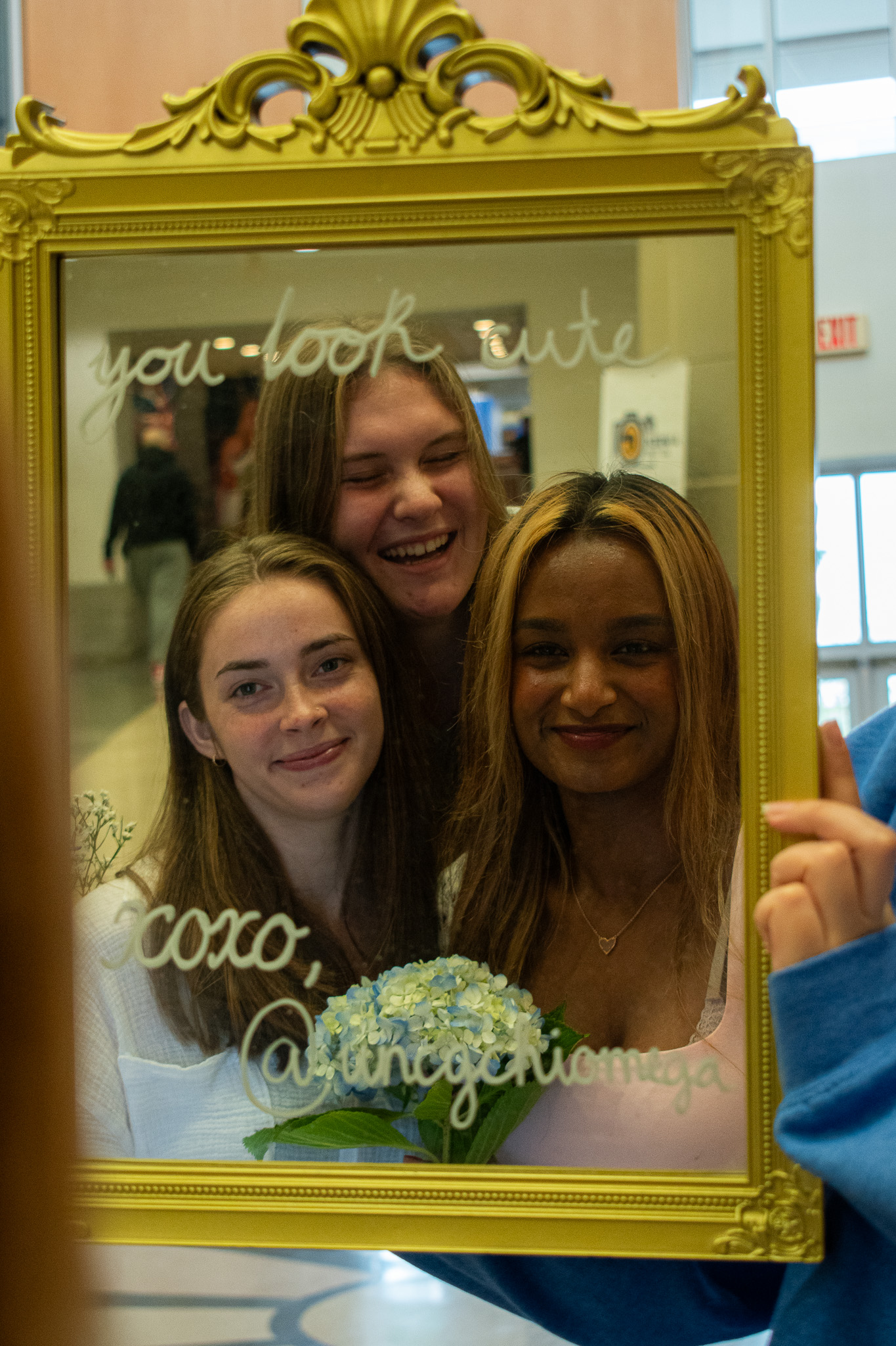 Photo of a gold mirror with three girls' reflections and messages on the mirror that read "You look cute. XOXO, Chi Omega"