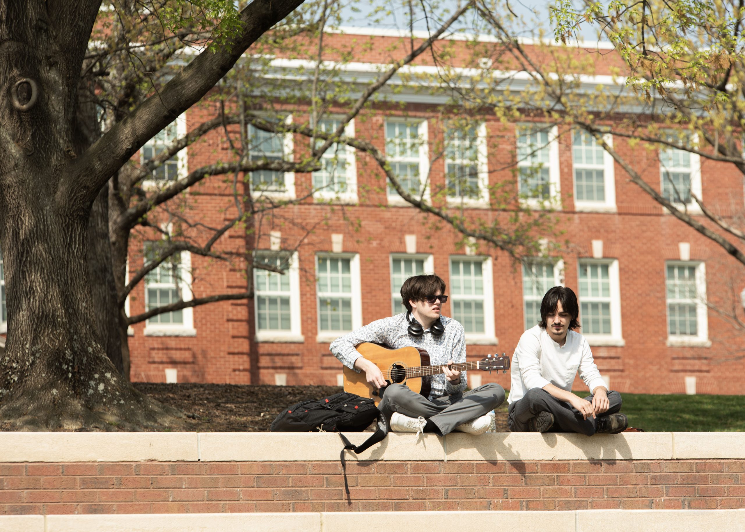 A student plays the guitar with another on the steps outside of Moran Commons.