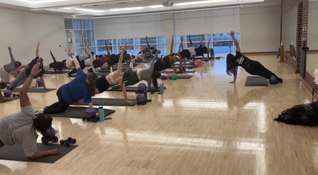 A room full of people stretch on yoga mats during a Pilates class.