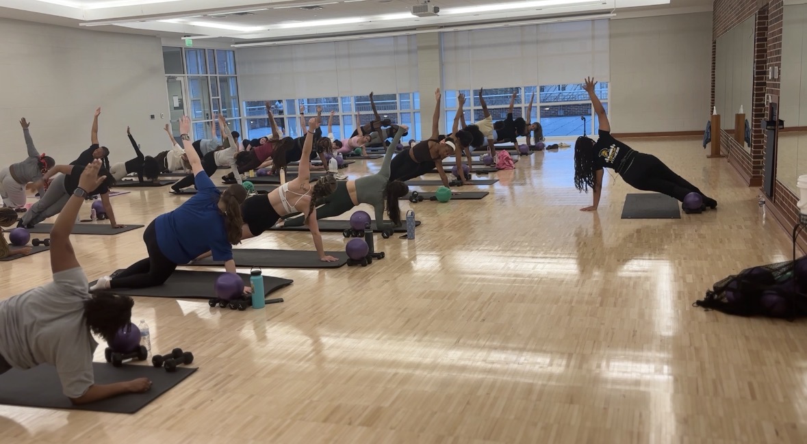 A room full of people stretch on yoga mats during a Pilates class.
