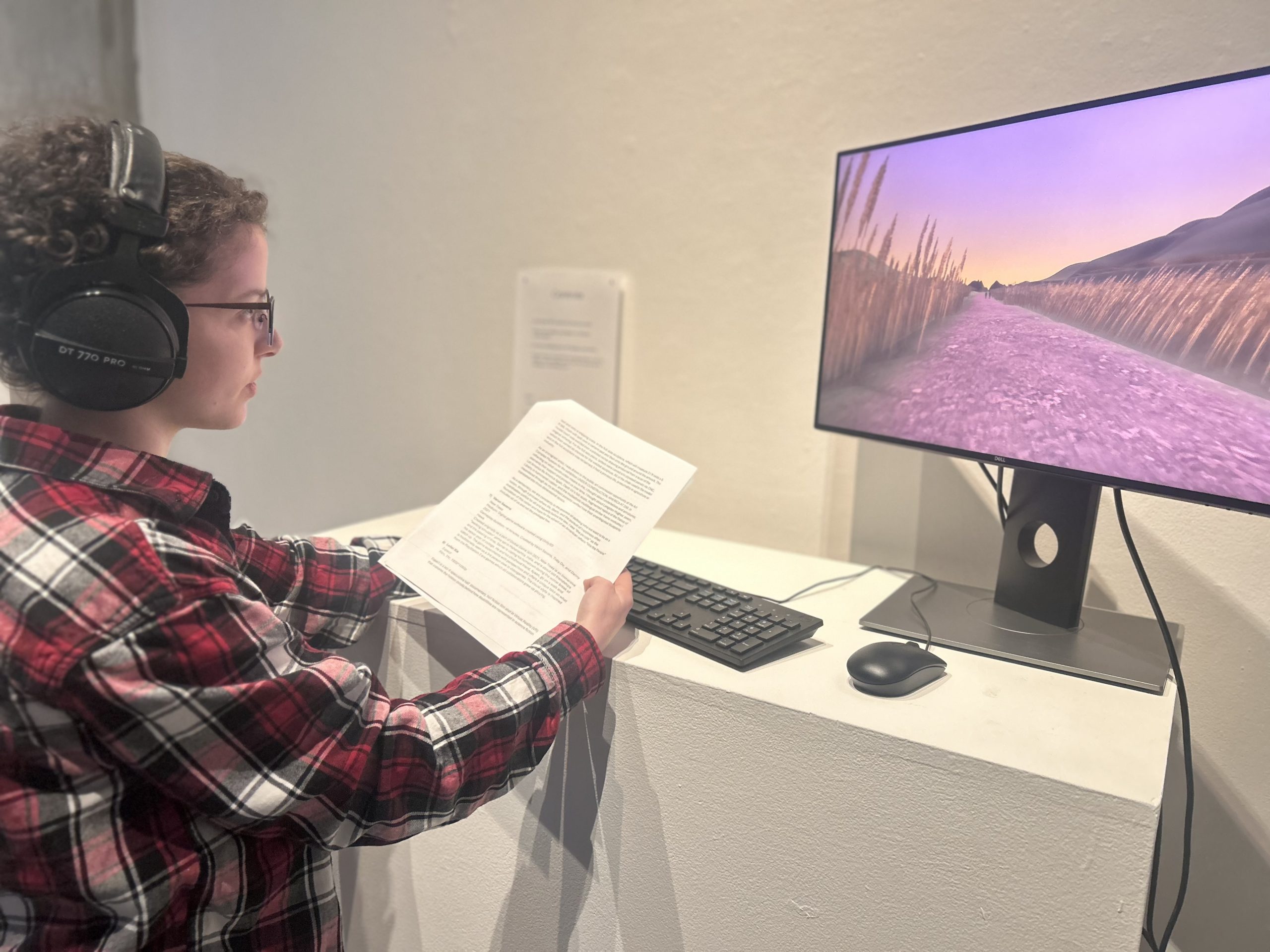 Student in headphones works on a keyboard and monitor displayed in an art gallery.