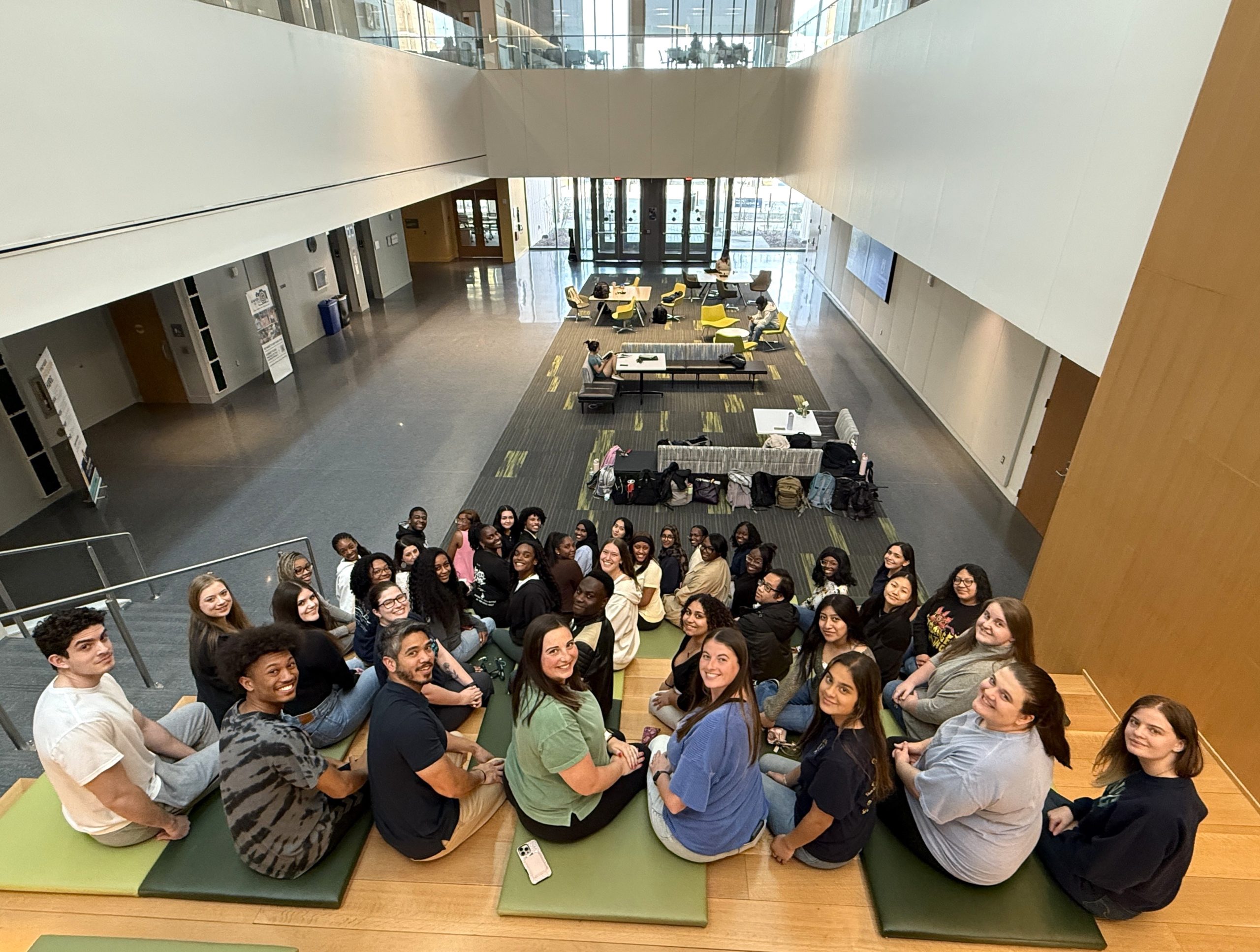 A group of students sit on the stairatorium in the NIB and look back at the camera.