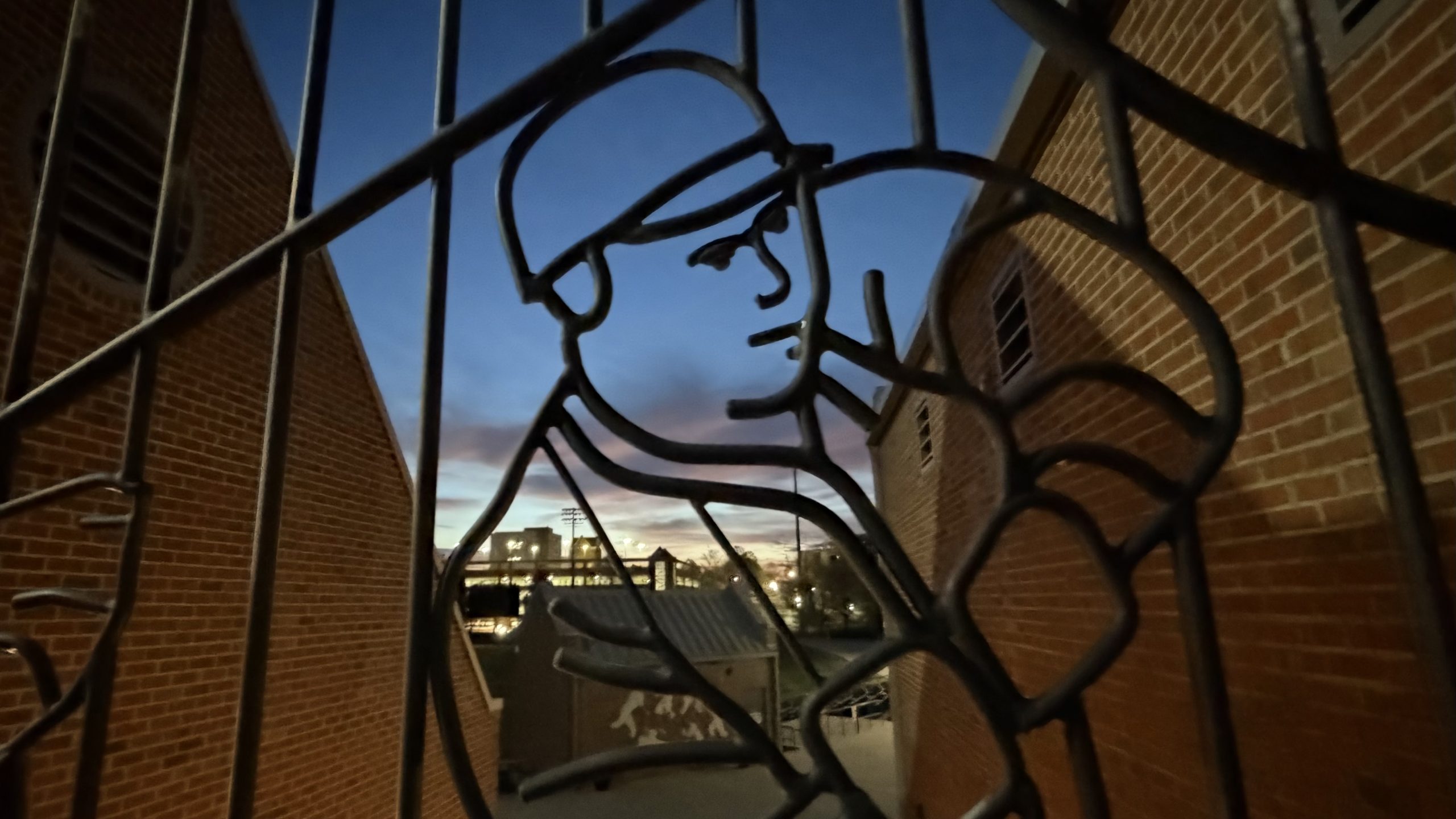 Sunrise over campus through baseball stadium gates.