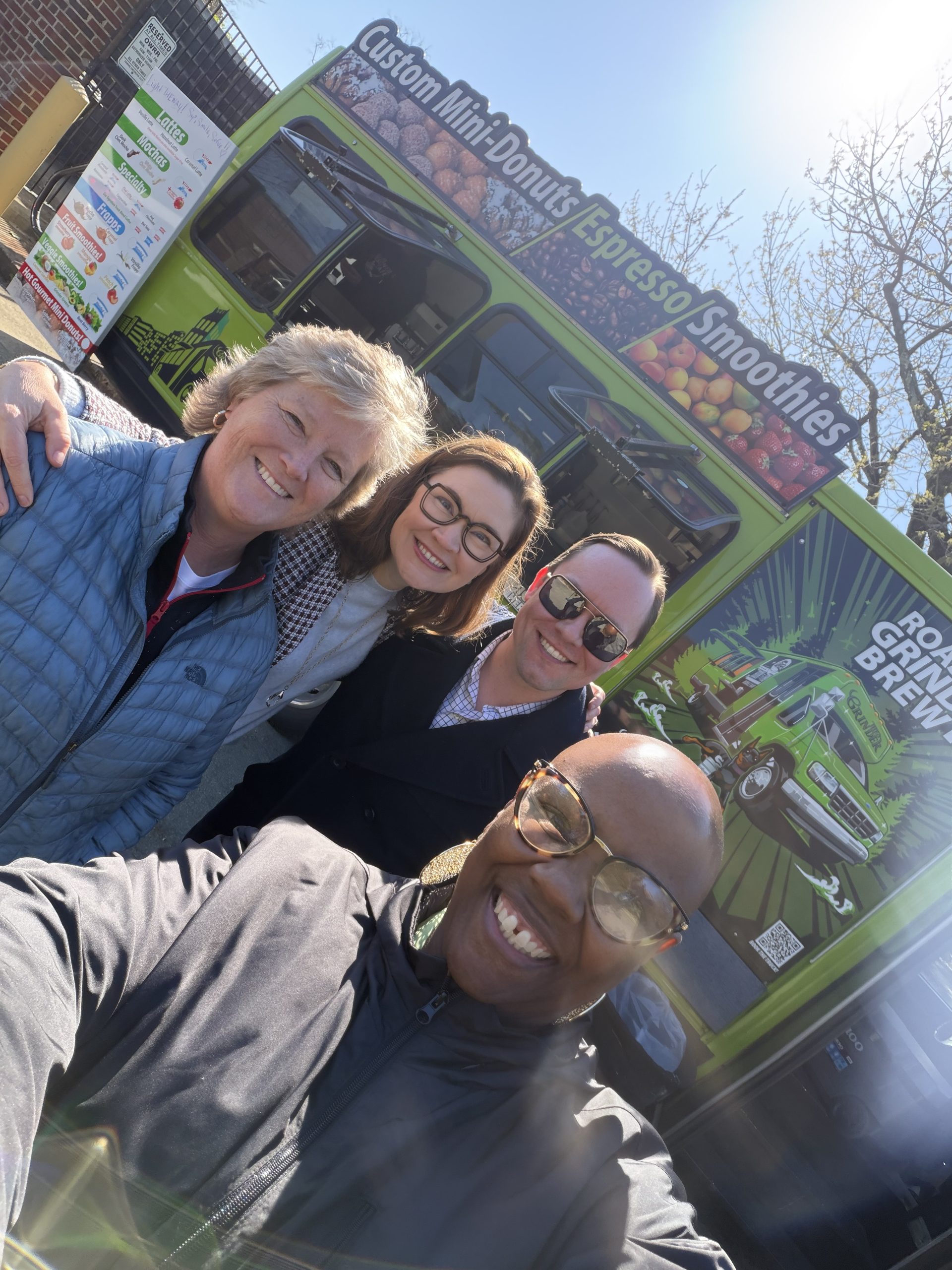 Four people standing in front of a food truck pose for group selfie.