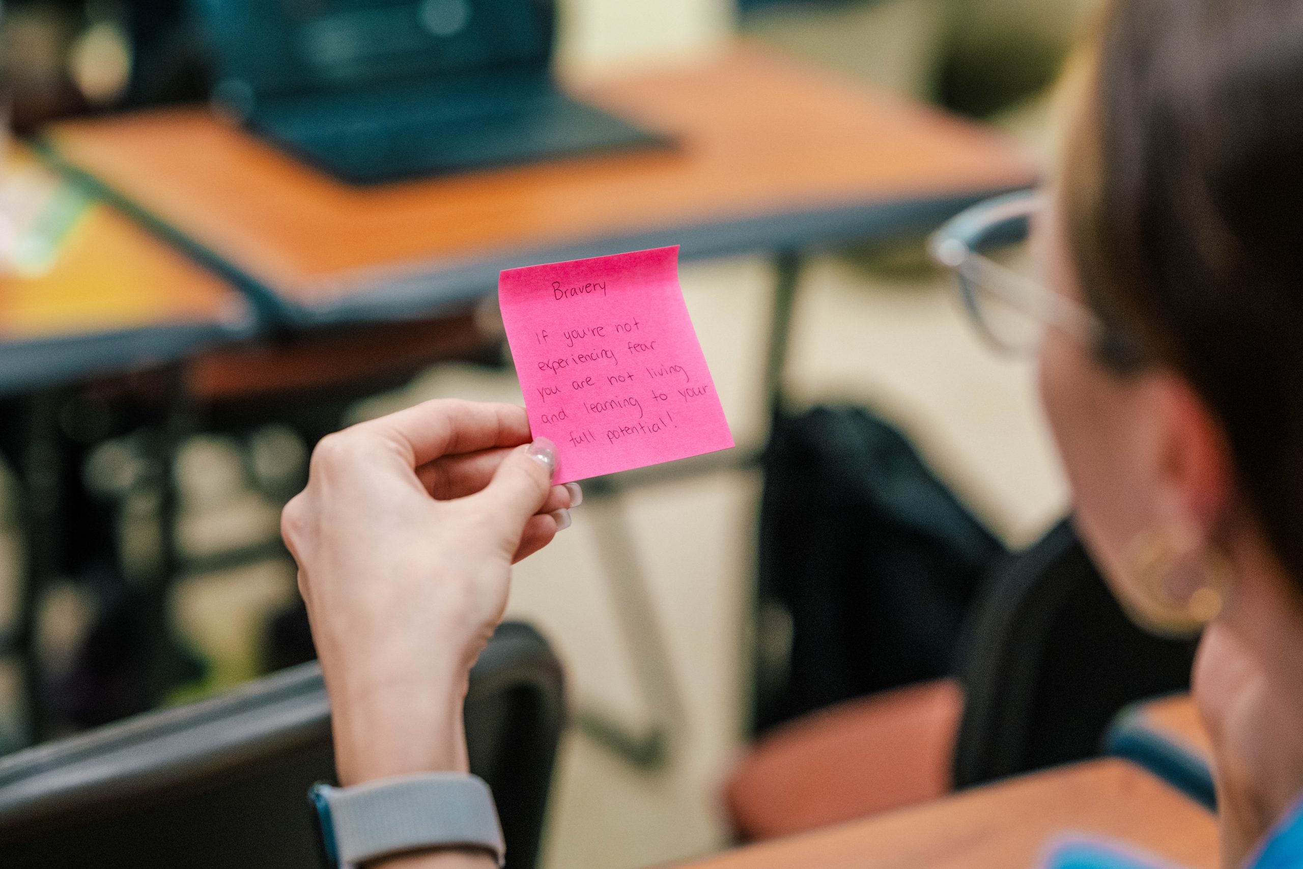 A person holding a pink sticky note that says, "Bravery — If you are not experiencing fear you are not living and learning to your full potential!"