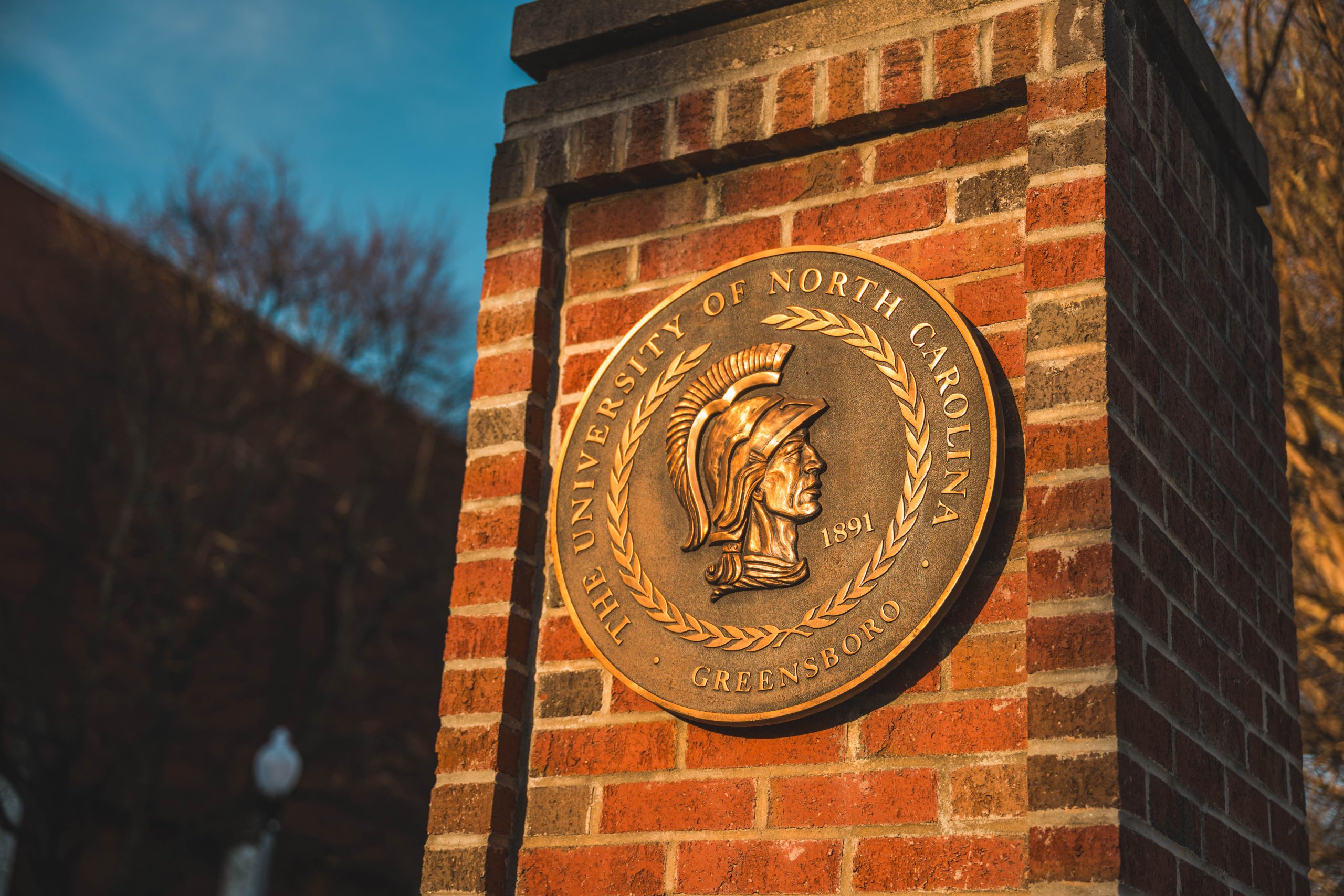 The UNC Greensboro seal at the entrance to campus catching first light as the sun rises on campus.