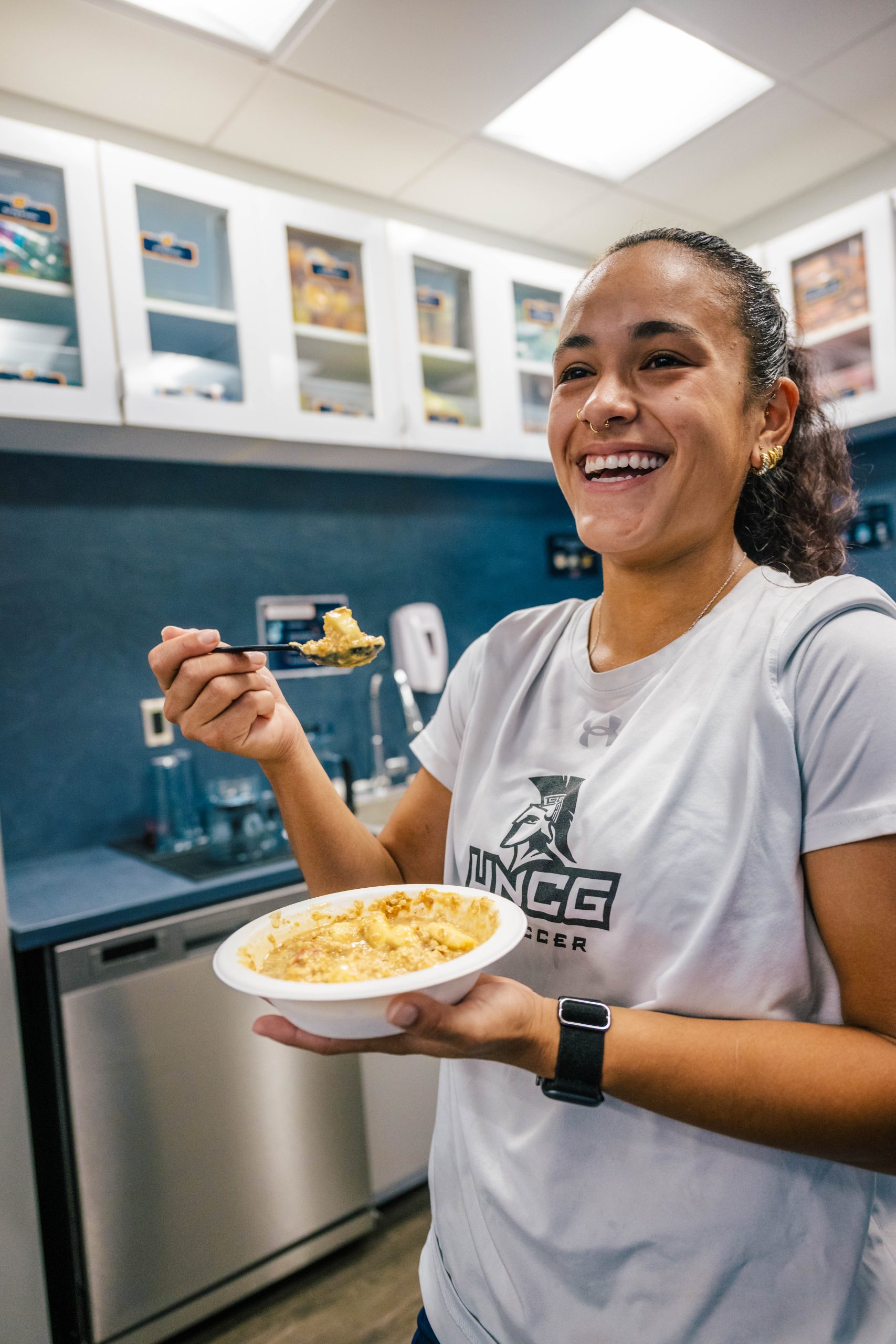 UNCG student in a kitchen takes a bite from a bowl of granola & yogurt.